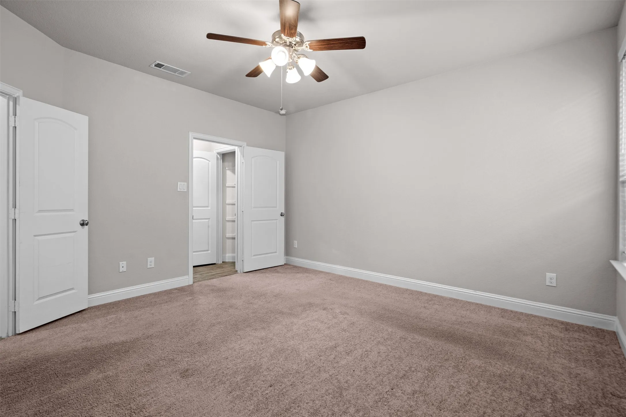 Spacious room featuring neutral carpet flooring, light gray wall paint, white baseboards, and a ceiling fan with light fixture