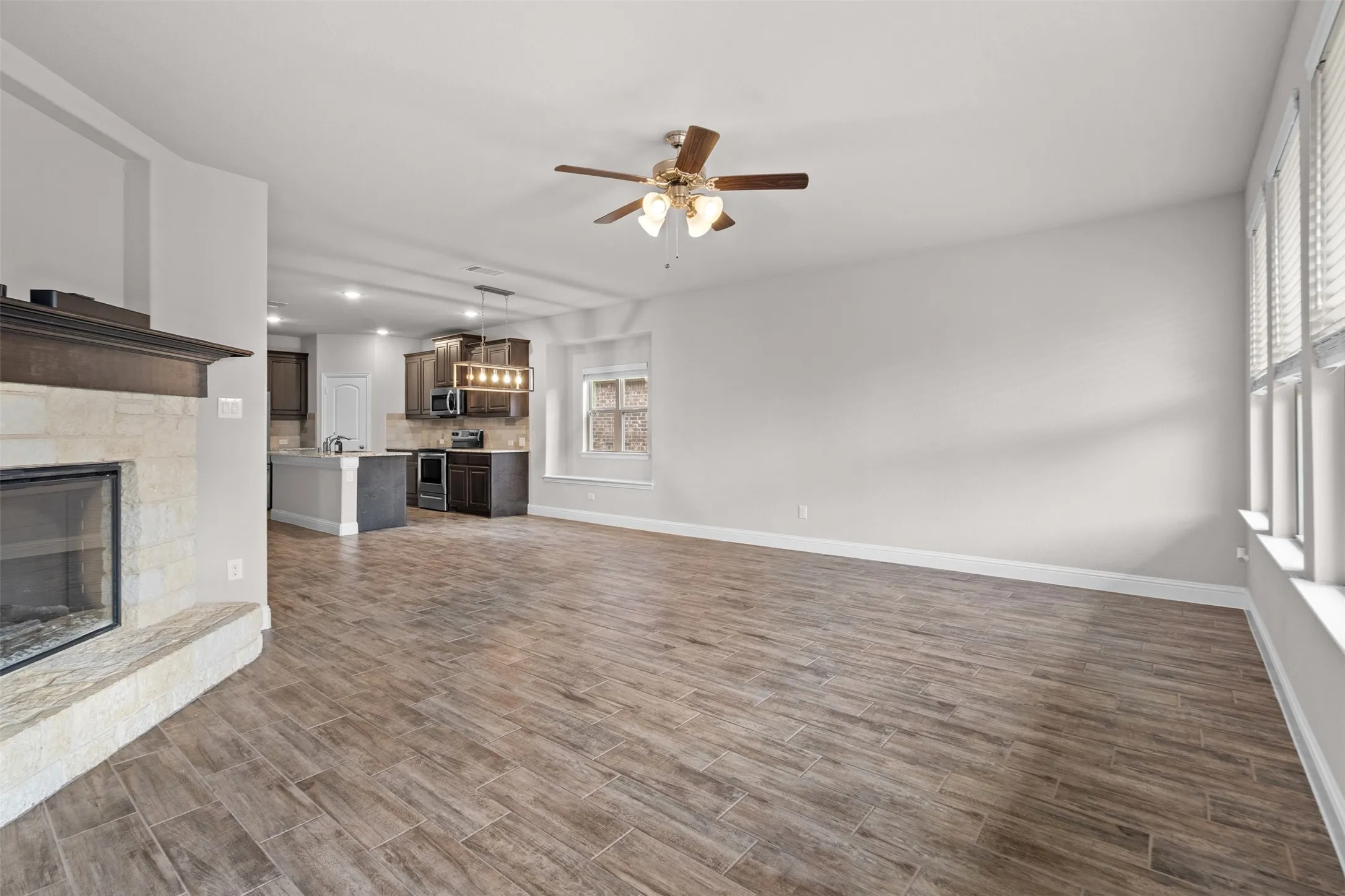 Spacious living area featuring wood-finish flooring and a stone-clad fireplace with a dark wood mantle