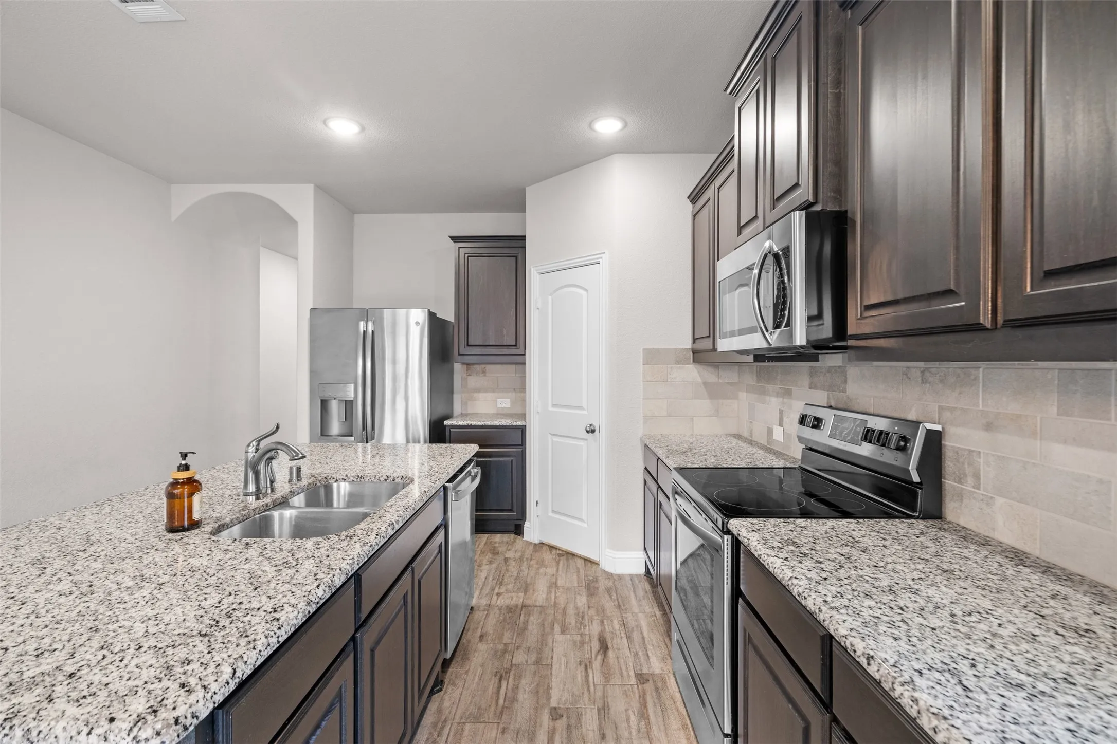 Kitchen featuring granite countertops, dark wood cabinetry, stainless steel appliances, wood-finish flooring, and a subway tile backsplash