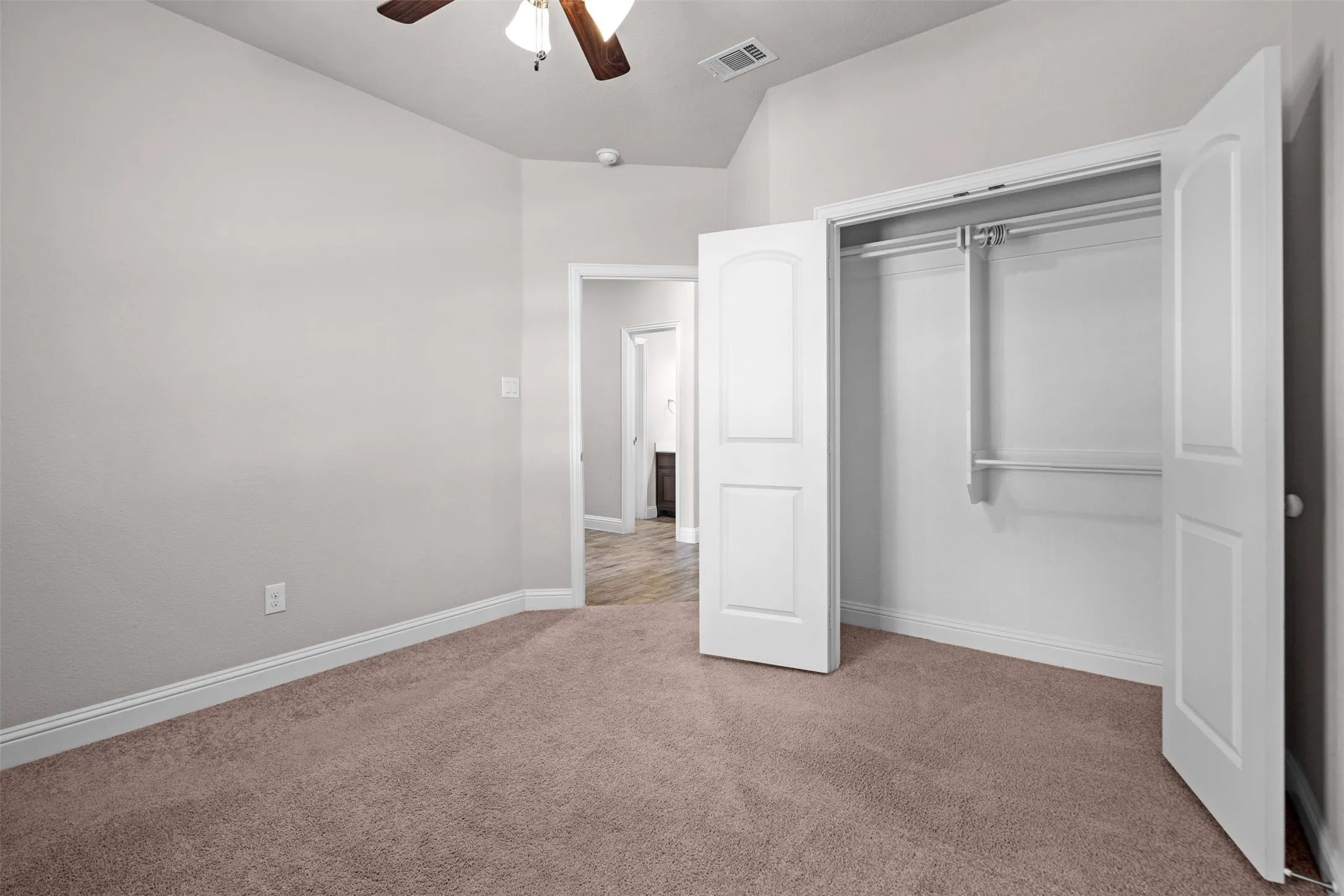 Carpeted room featuring a ceiling fan with light fixture, vaulted ceiling, and base molding