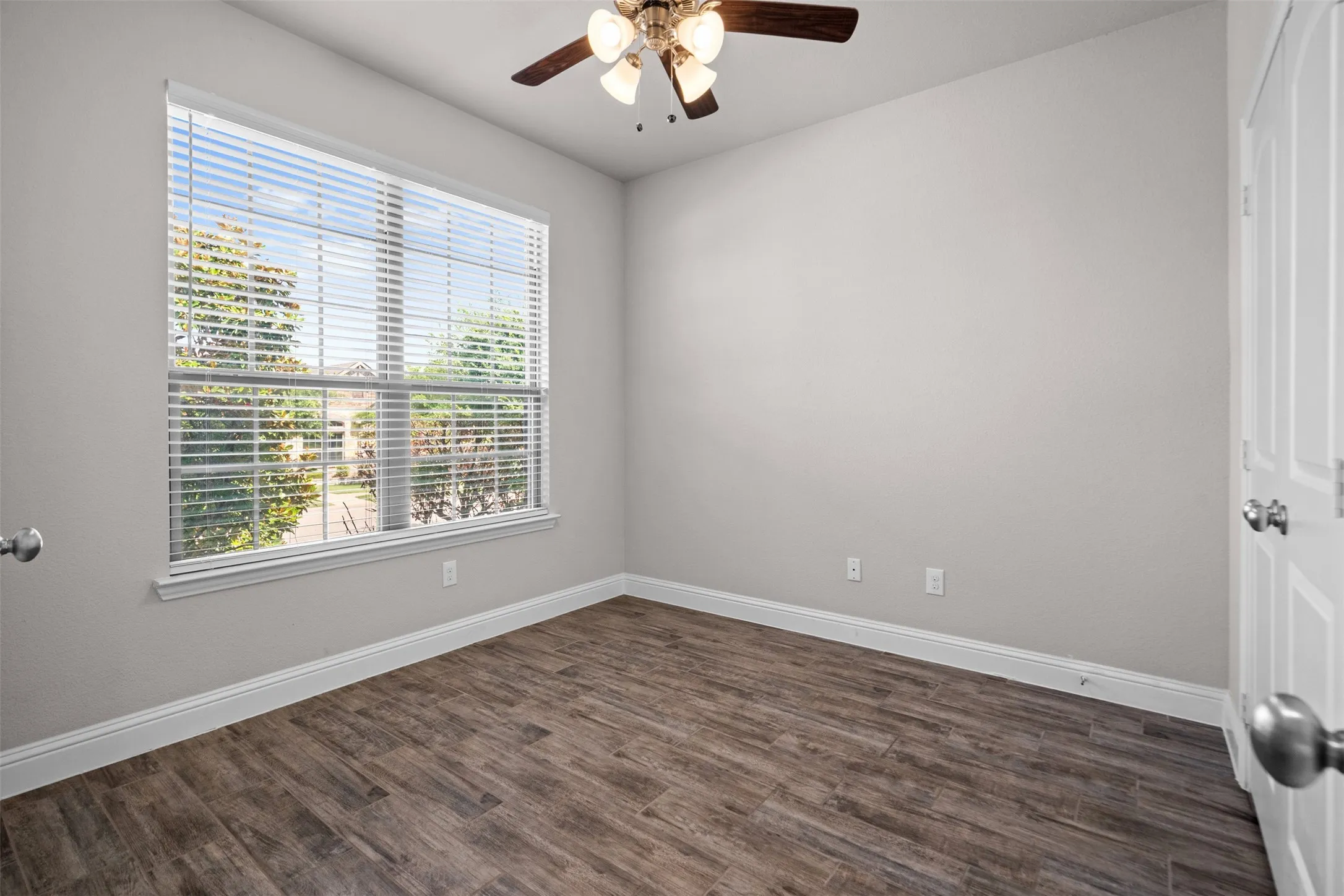 Neutral wall tones featuring a window with horizontal blinds, wood-finish flooring, white baseboards, and a ceiling fan with integrated lighting