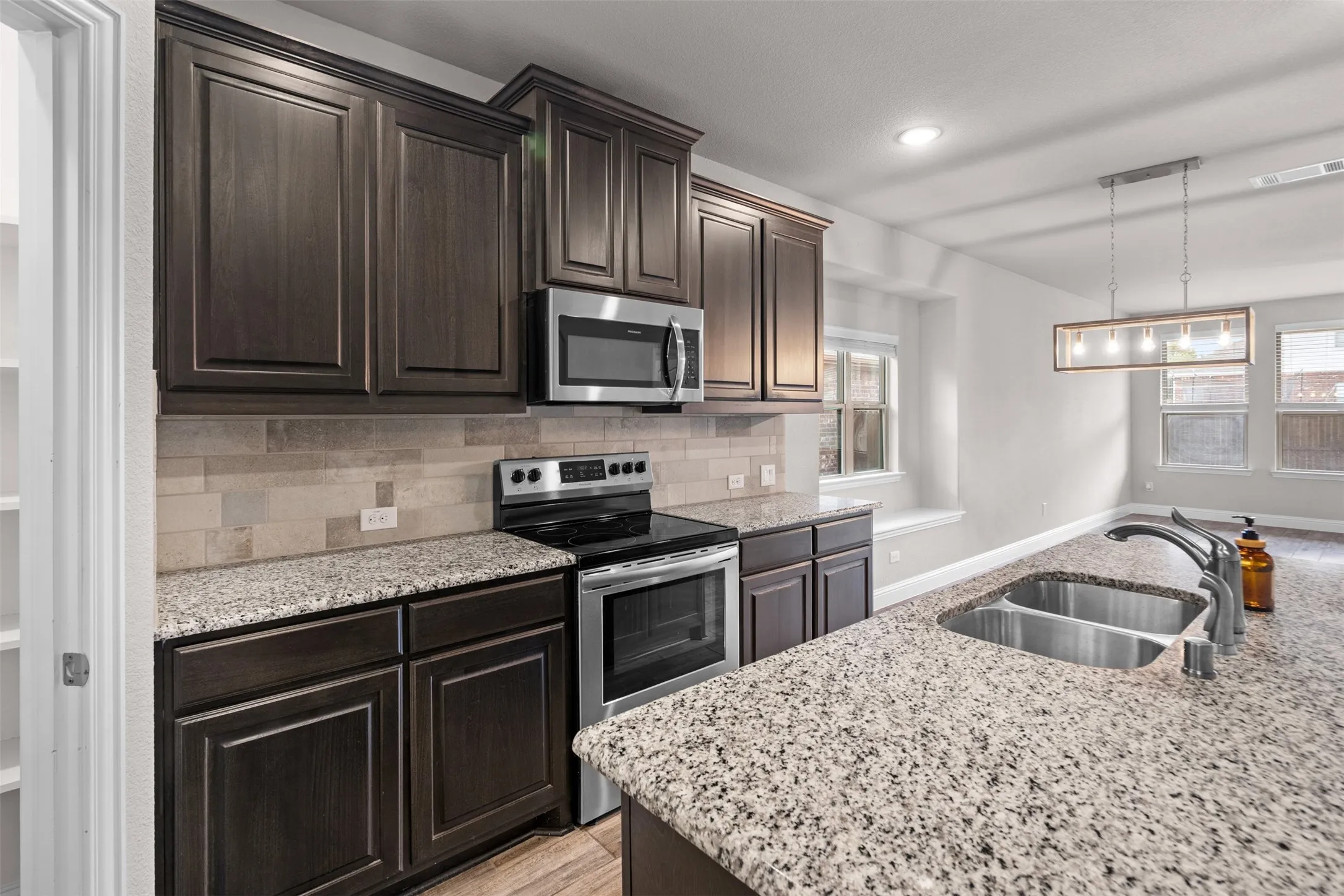 Kitchen featuring granite countertops, dark wood cabinetry, stainless steel appliances, a tile backsplash, and a double basin sink