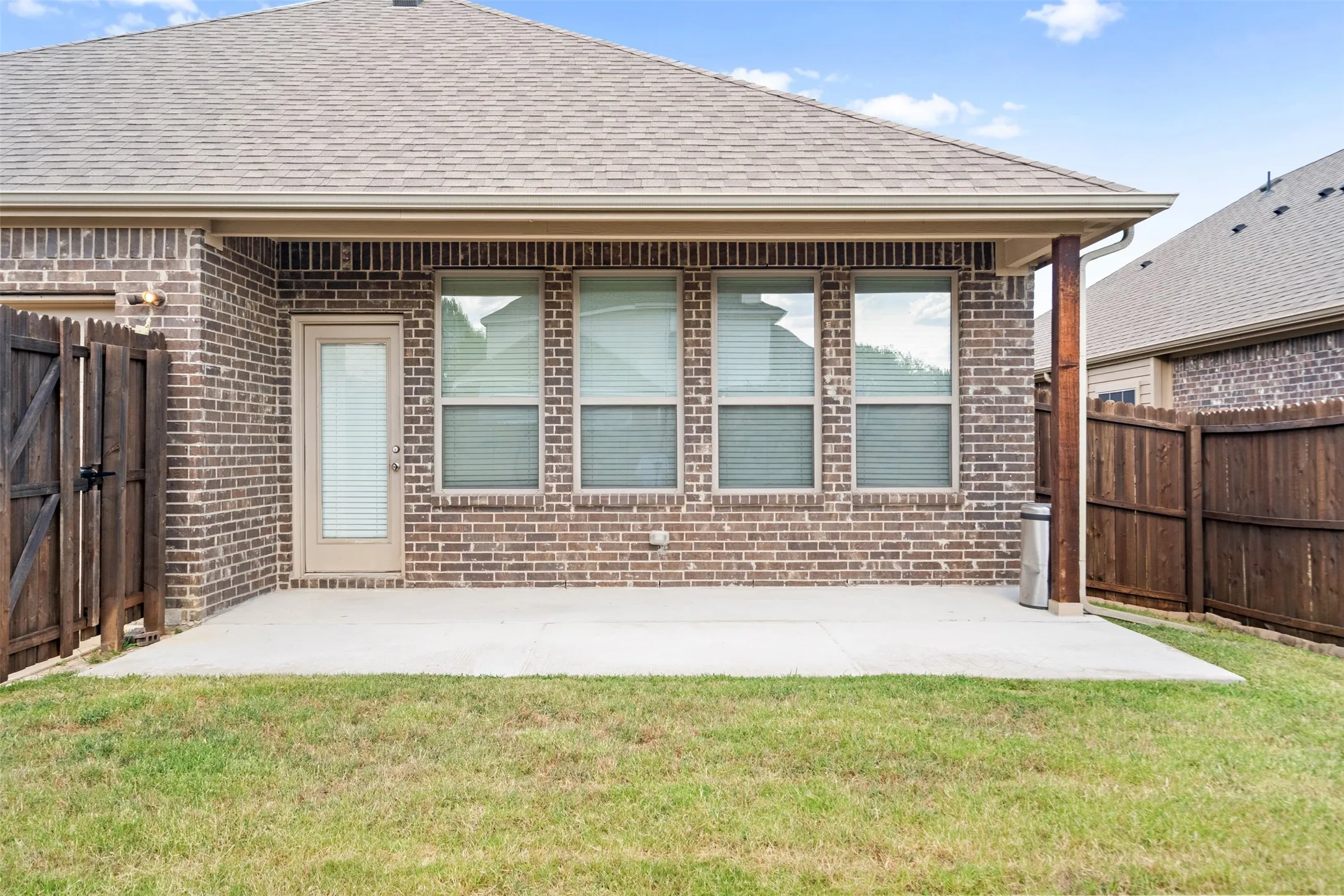 Covered patio area featuring a concrete slab, brick exterior, and a wood-paneled fence