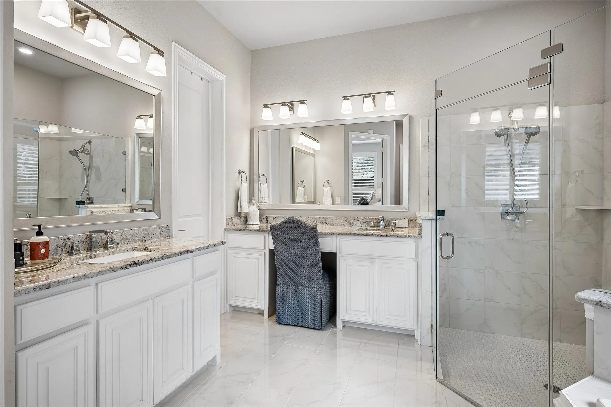 Spacious bathroom featuring a glass-enclosed shower with a tiled surround, dual vanity with undermount sinks, stone countertops, white cabinetry, and large format floor tiling