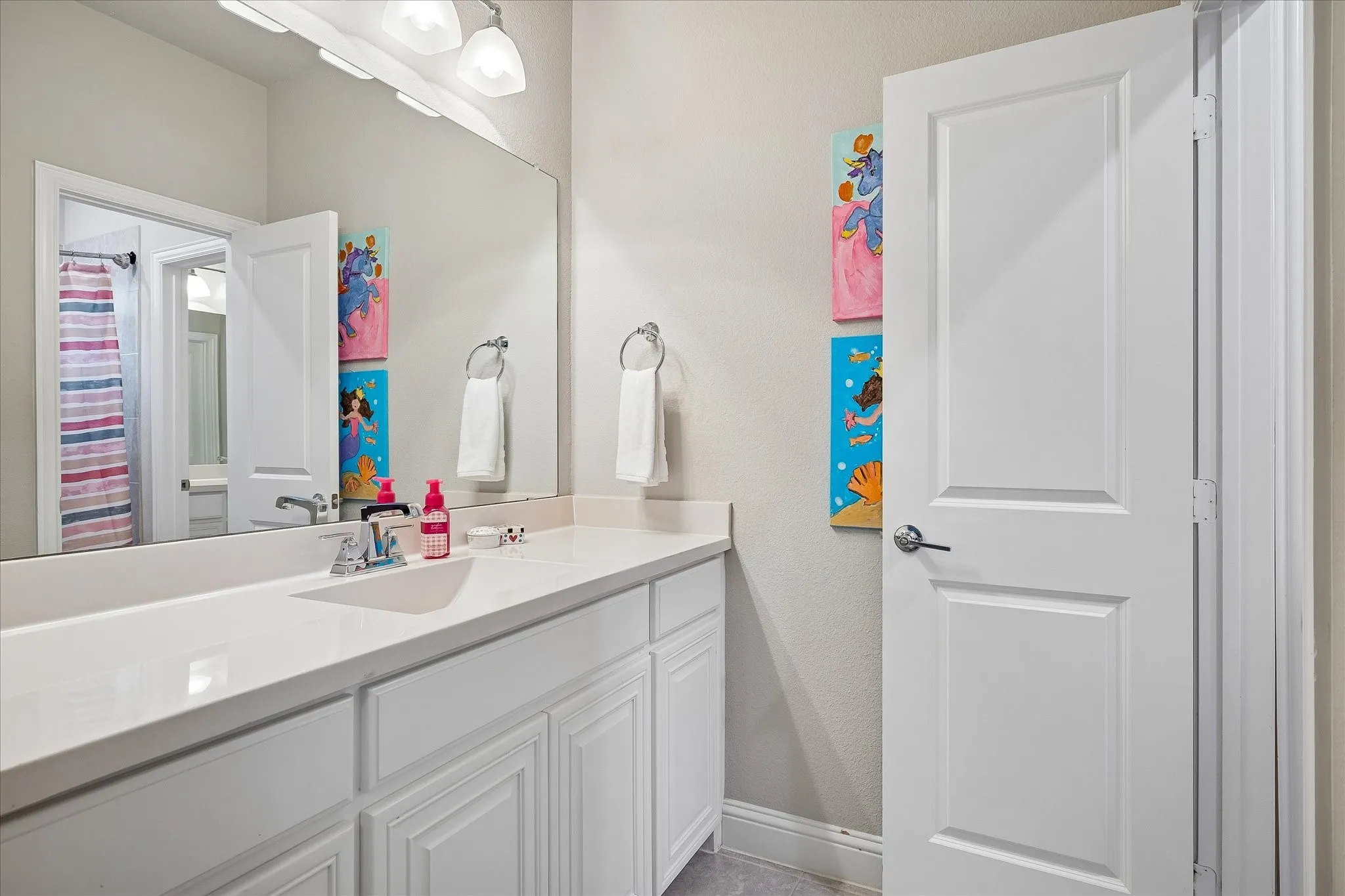Spacious bathroom featuring an extended vanity with a solid surface countertop, an integrated sink basin, white cabinetry, and a large mirror