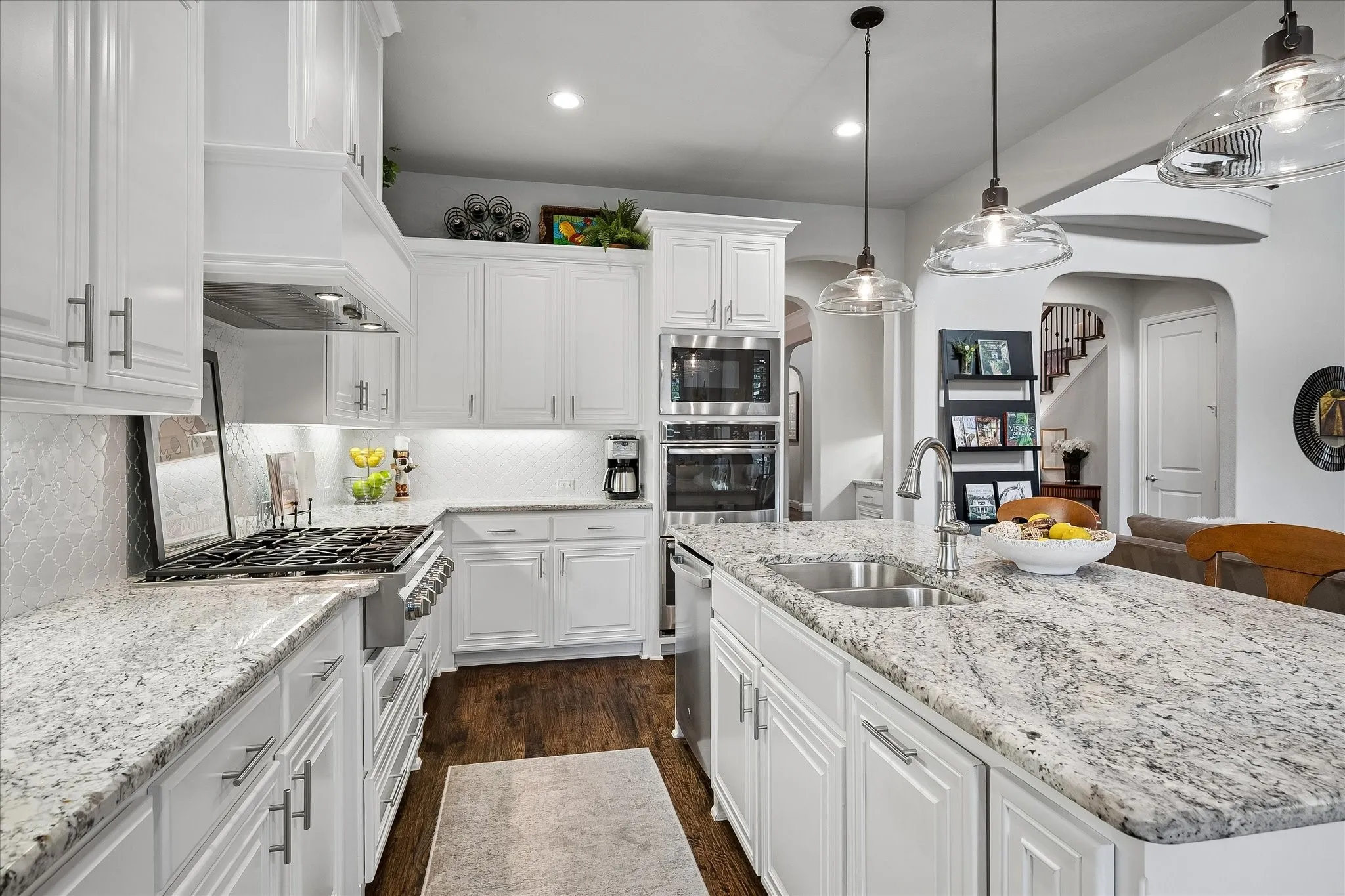 Bright kitchen featuring white cabinetry, stone countertops, stainless steel appliances, a gas range with an overhead vent hood, and an island with an undermount sink