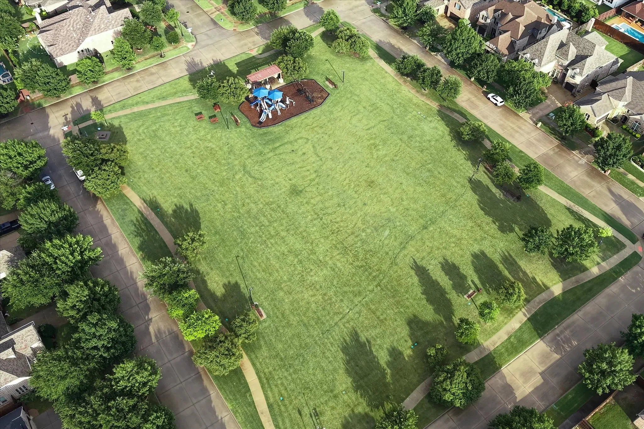 Expansive neighborhood park - Blue Park featuring a large grassy area, a dedicated playground with structures, multiple park benches, and a walking path surrounding the perimeter