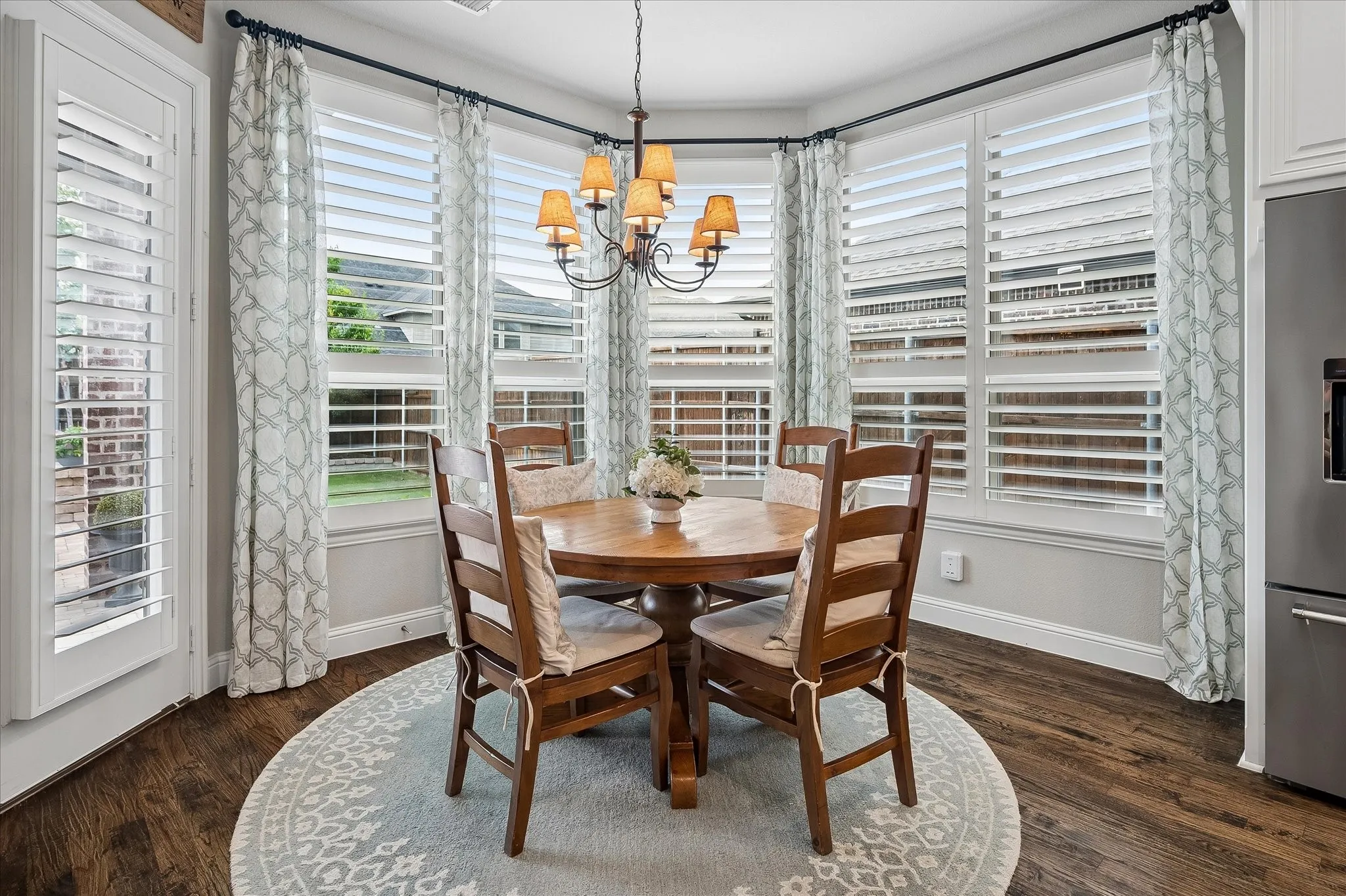 Bay window dining area with plantation shutters, dark wood-finish flooring, and an ornamental chandelier