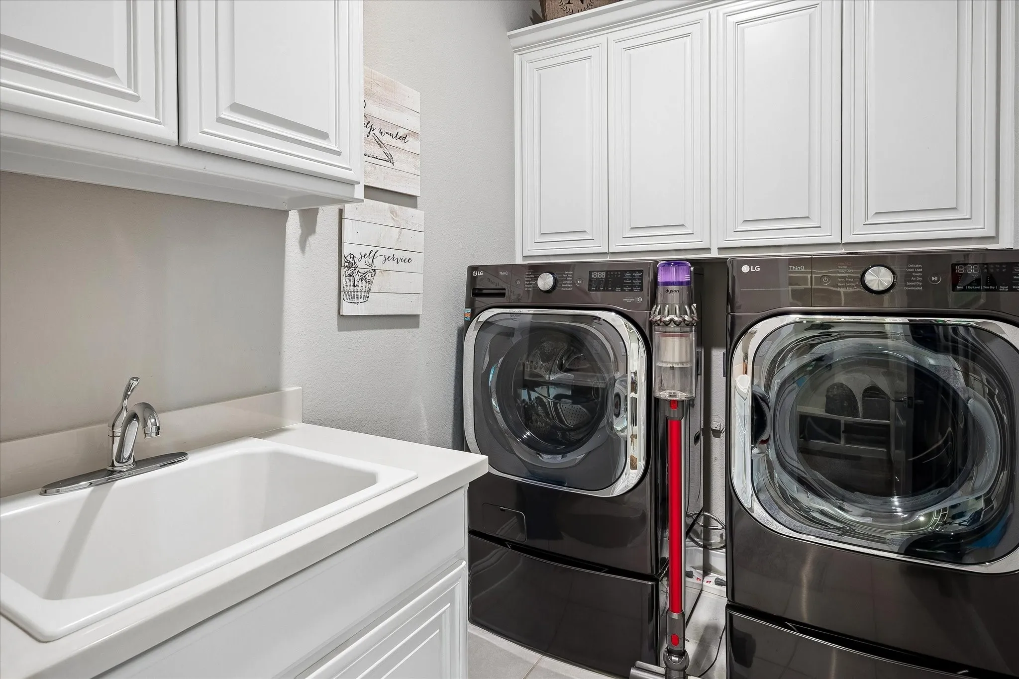 Laundry area featuring white cabinetry, a utility sink with a chrome faucet, and ample counter space