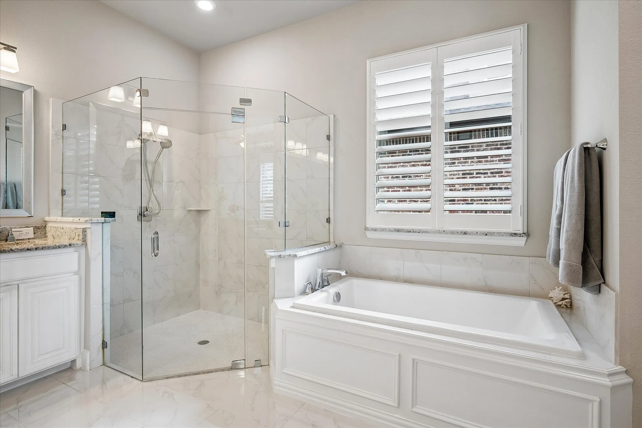 Spacious bathroom featuring a glass-enclosed shower with tile surround, a built-in soaking tub with paneled apron, white plantation shutters, and light-toned tile flooring