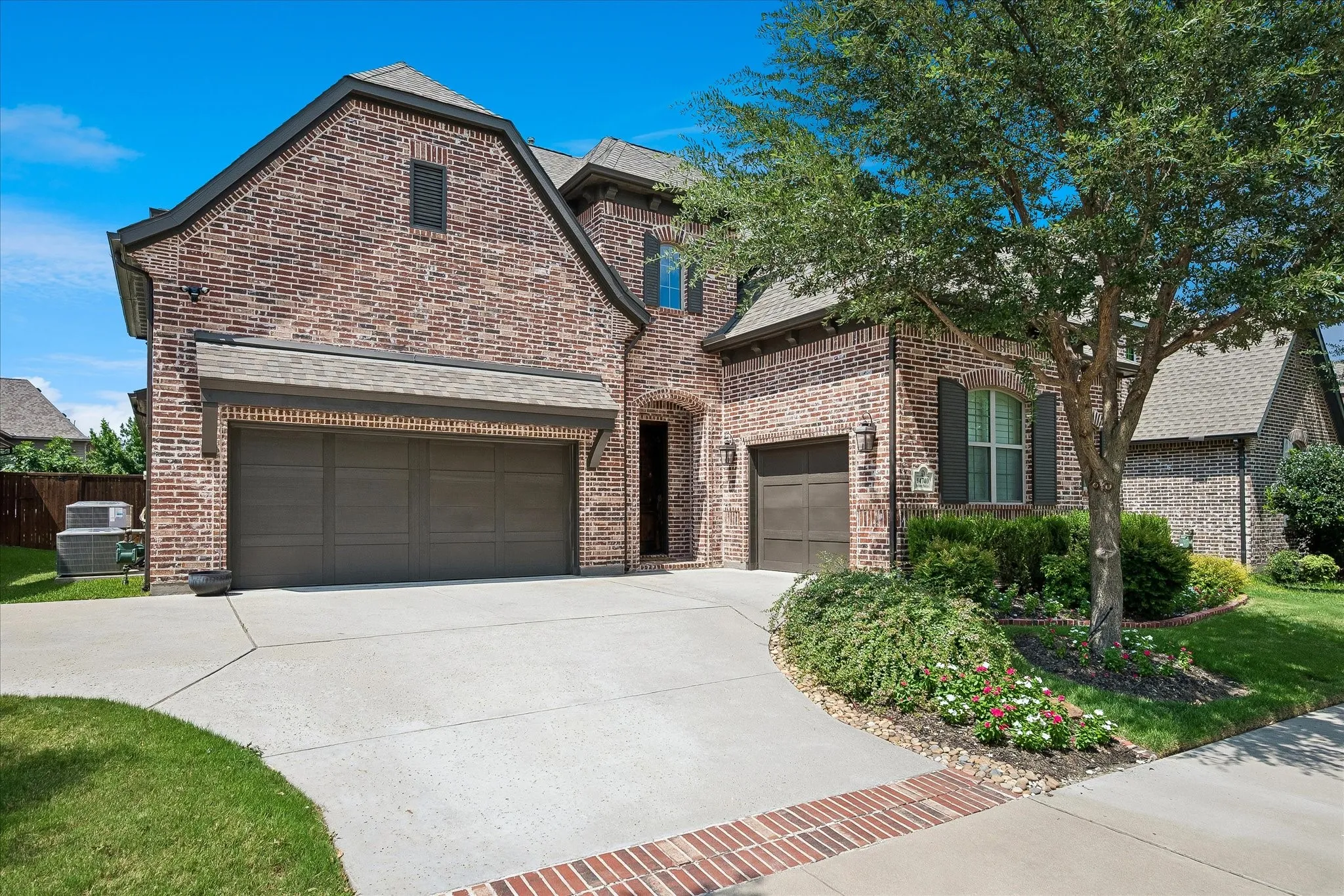 Brick exterior featuring a multi-car garage, mature landscaping, and a concrete driveway with brick accents