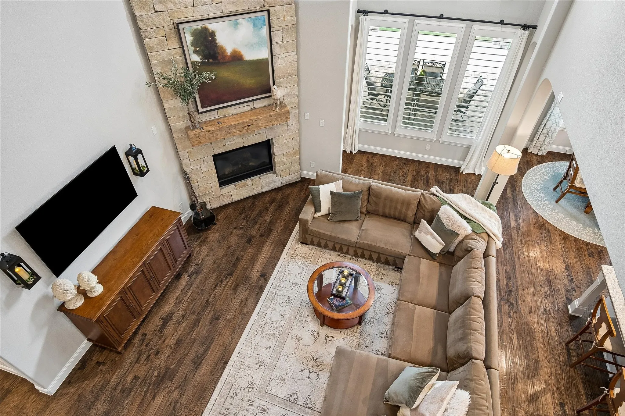 Living area featuring a stone-clad fireplace with a wood mantel, multi-paned windows with plantation shutters, high ceilings, and wood-finish flooring