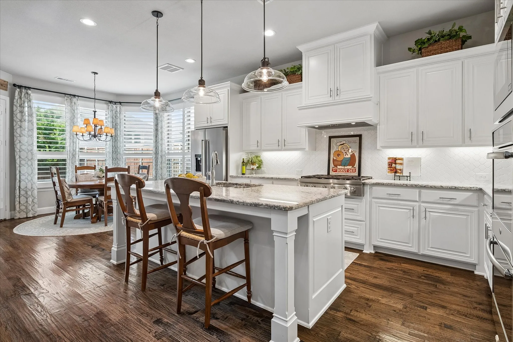 Open-concept kitchen featuring white cabinetry, light countertops, wood-finish flooring, and a dining area with bay windows