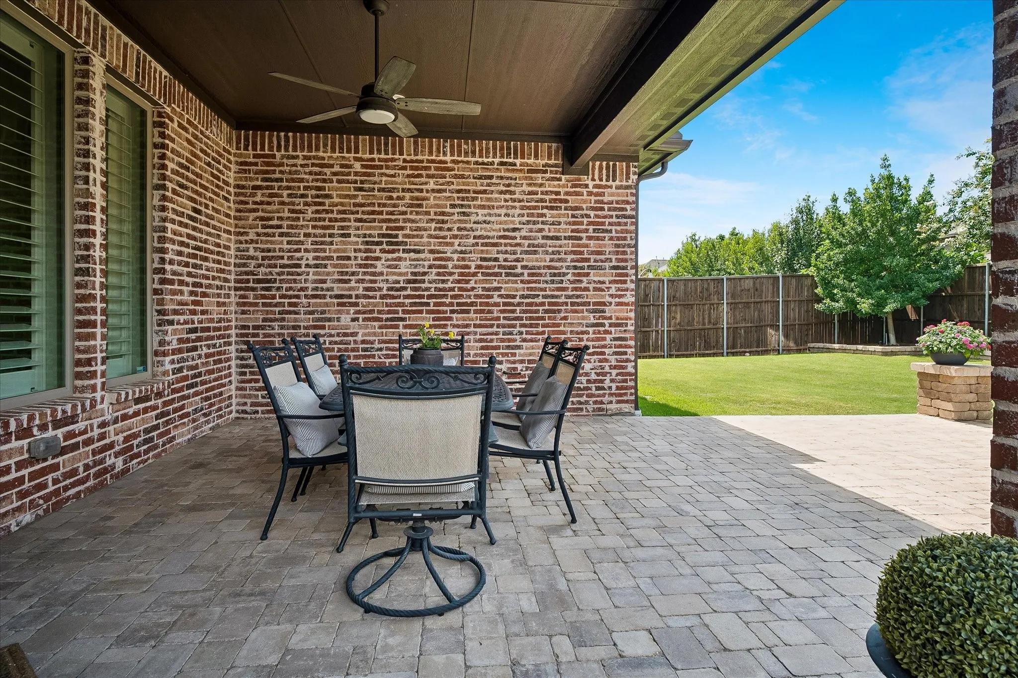 Covered patio featuring brick exterior, paver flooring, and ceiling fan