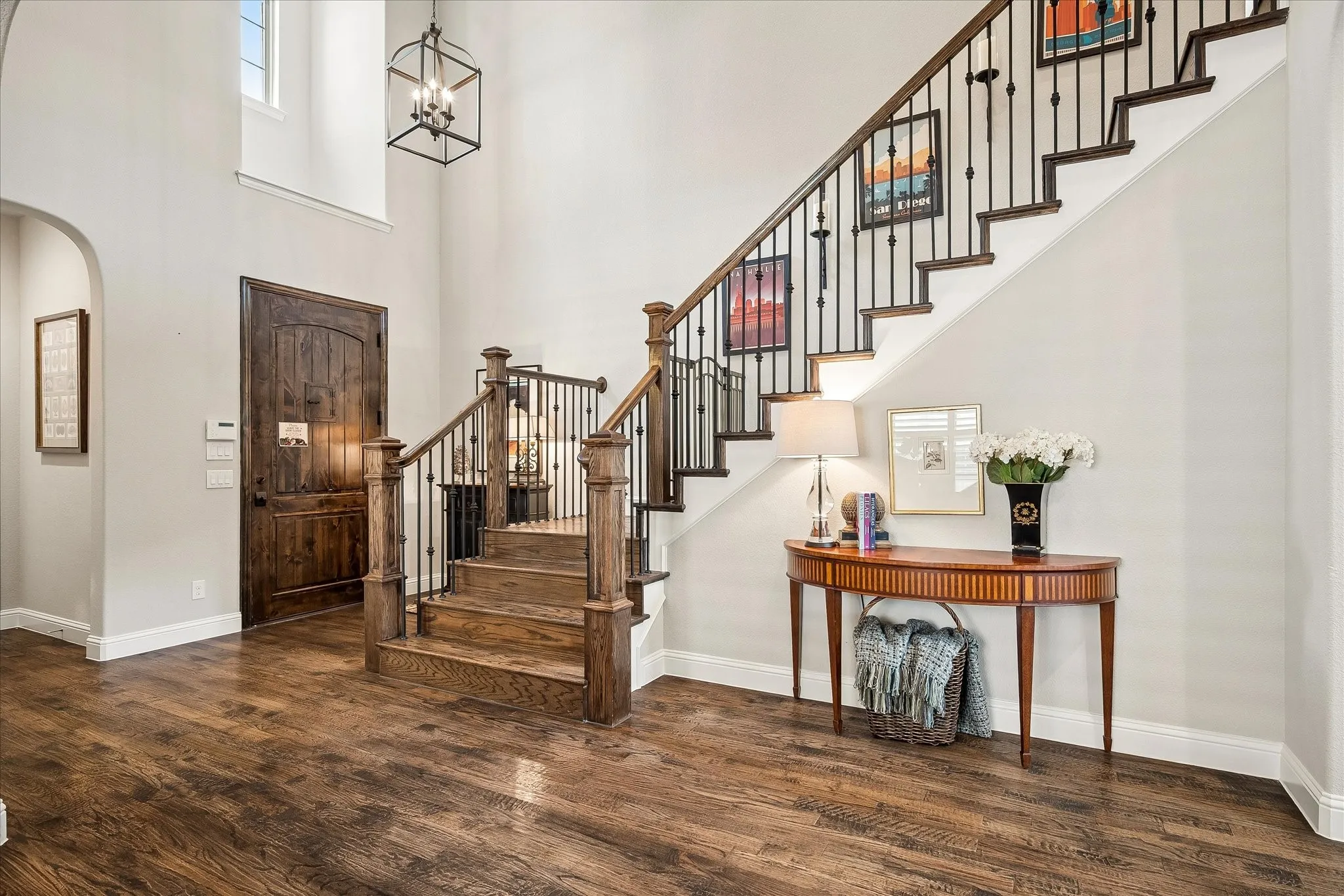 Grand entryway featuring a two-story ceiling, wood-finish flooring, a prominent staircase with dark wood newel posts and iron balusters, a large archway, and an ornate wooden door