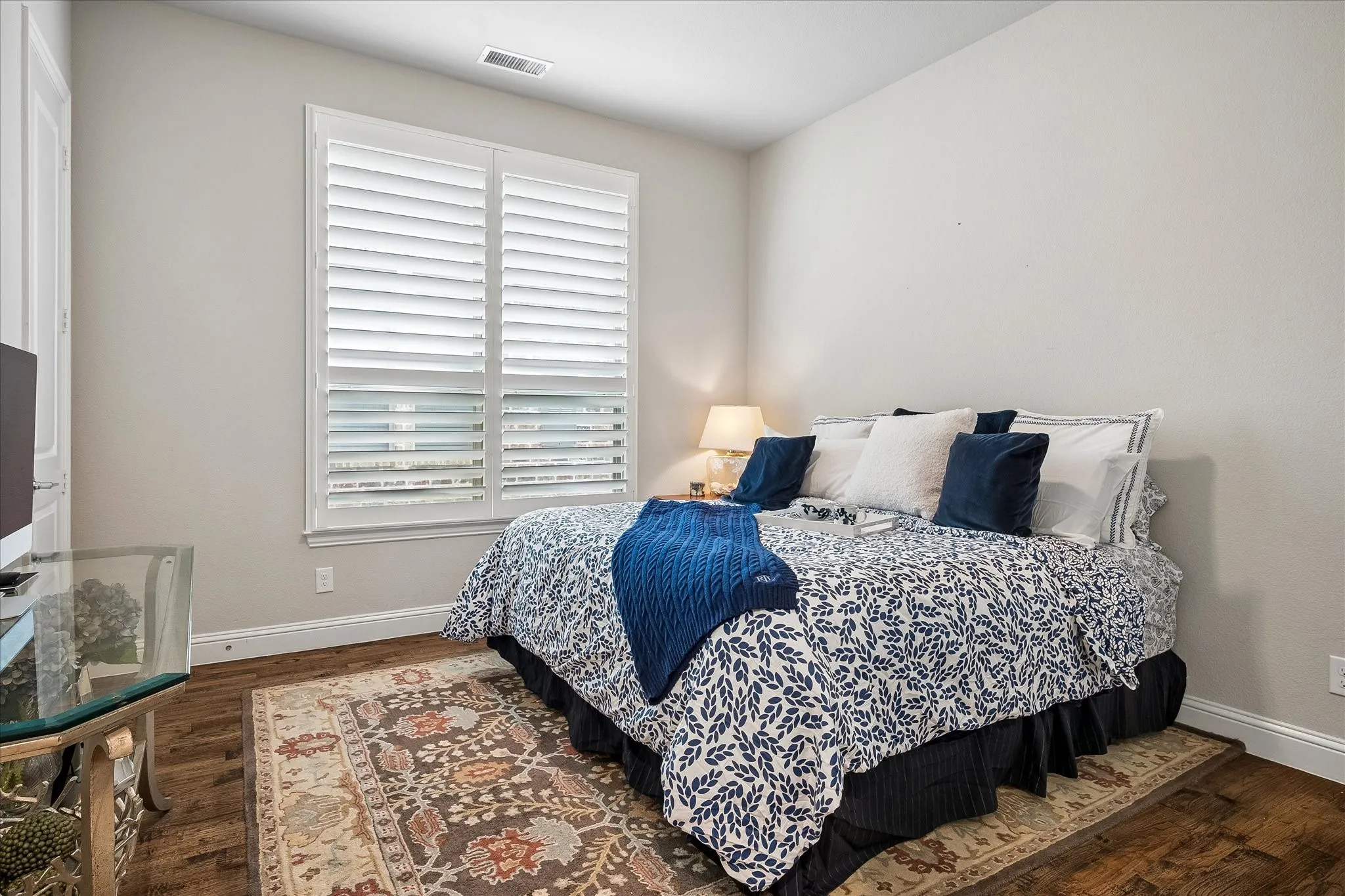 Bedroom with wood-finish flooring, light neutral wall paint, and white plantation shutters