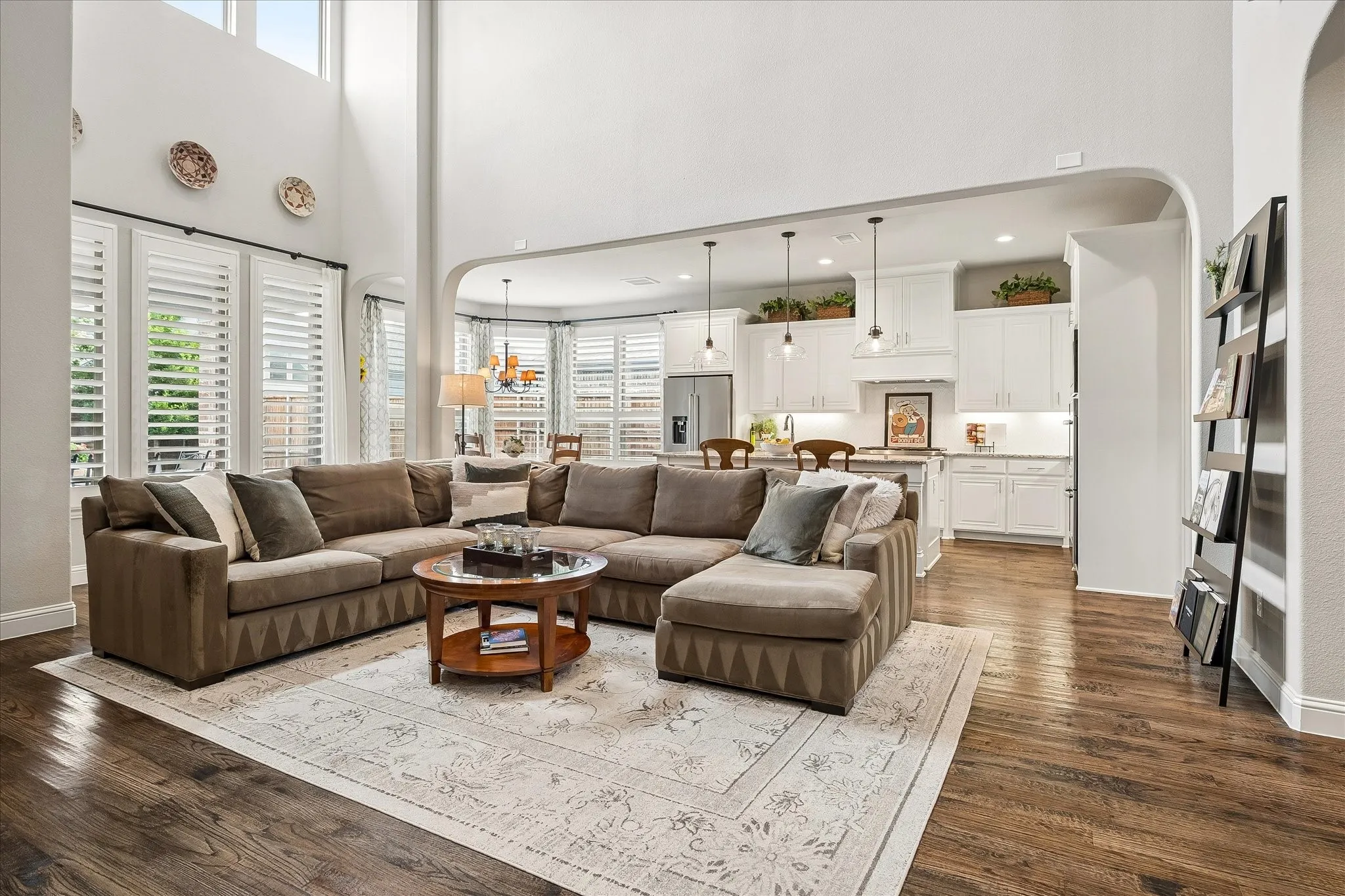 Two-story living area with high ceilings, wood-finish flooring, and white plantation shutters