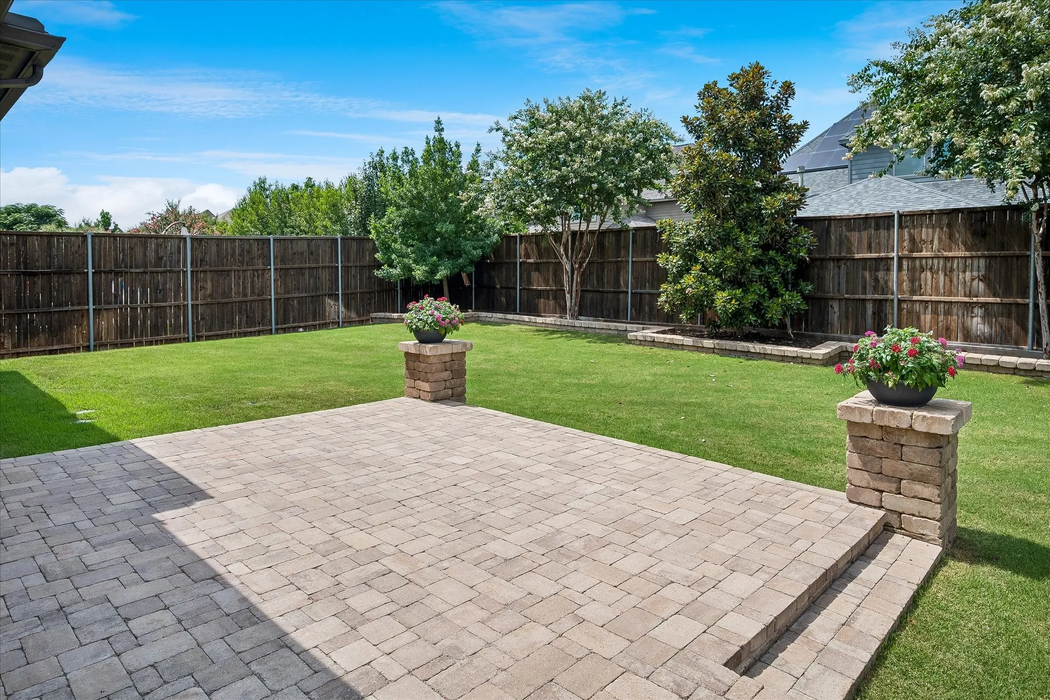 Expansive backyard featuring a paver patio with integrated steps, a manicured lawn, and perimeter wood fencing