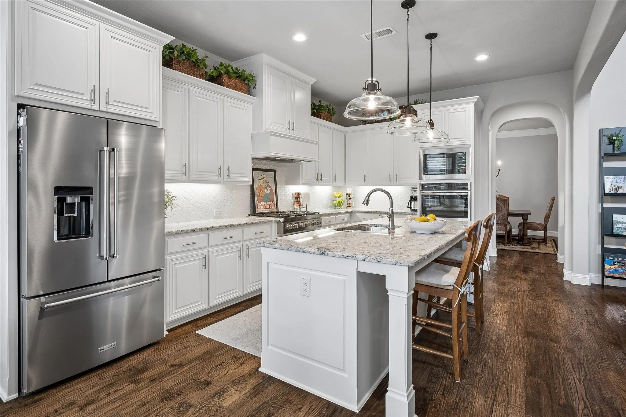 Gourmet kitchen with white cabinetry, stainless steel appliances, granite countertops, and wood-finish flooring