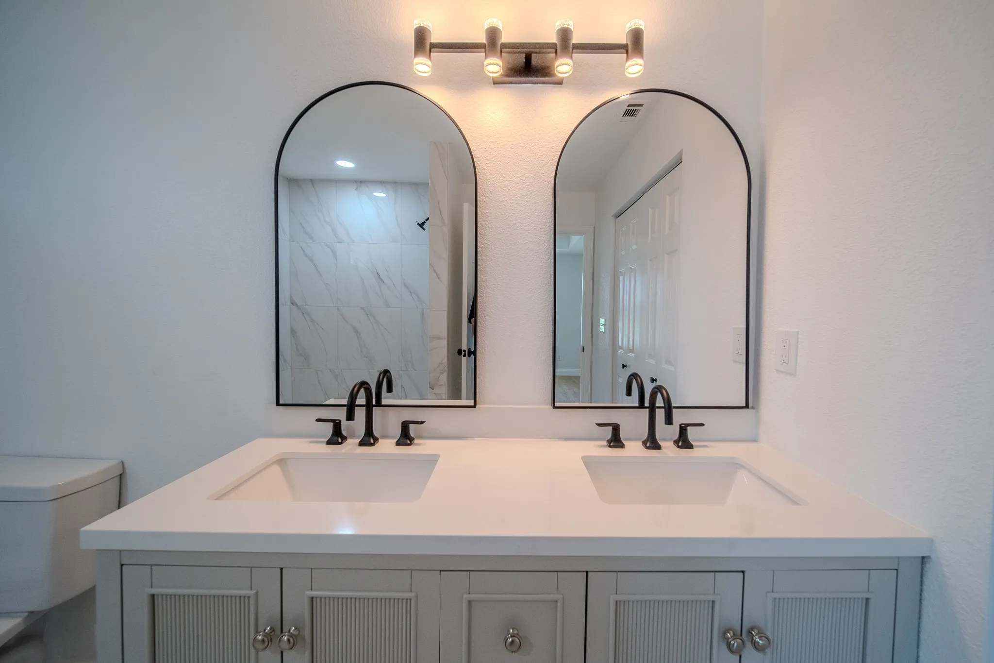 Bathroom vanity featuring dual arched mirrors, a light-toned countertop, and matte black fixtures