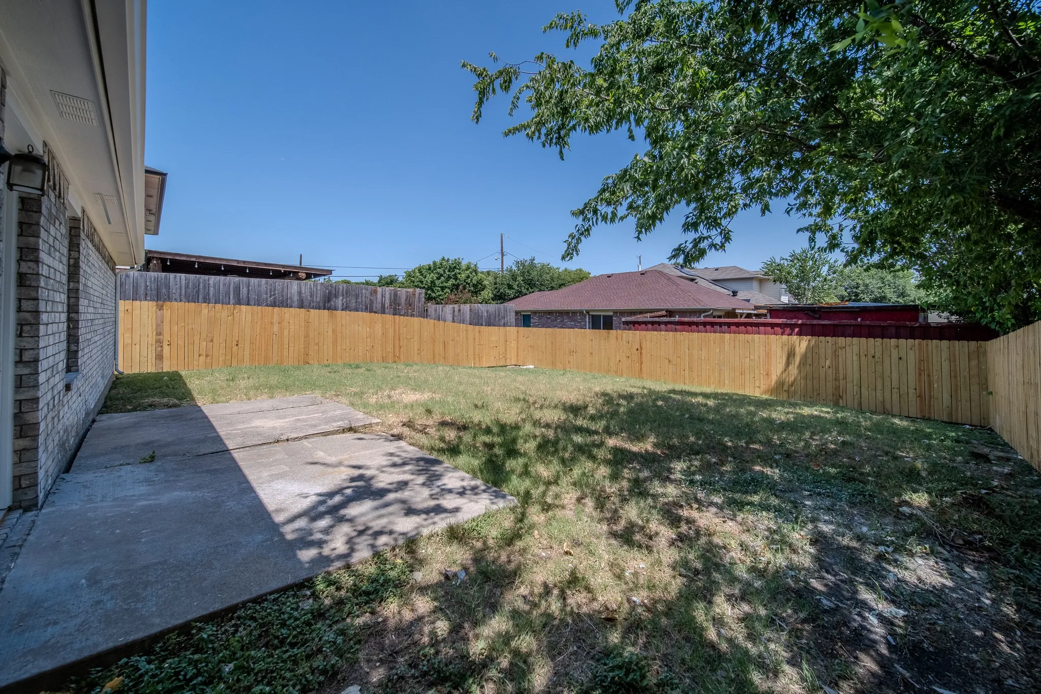 Expansive backyard featuring a new wood fence, mature tree, and concrete patio