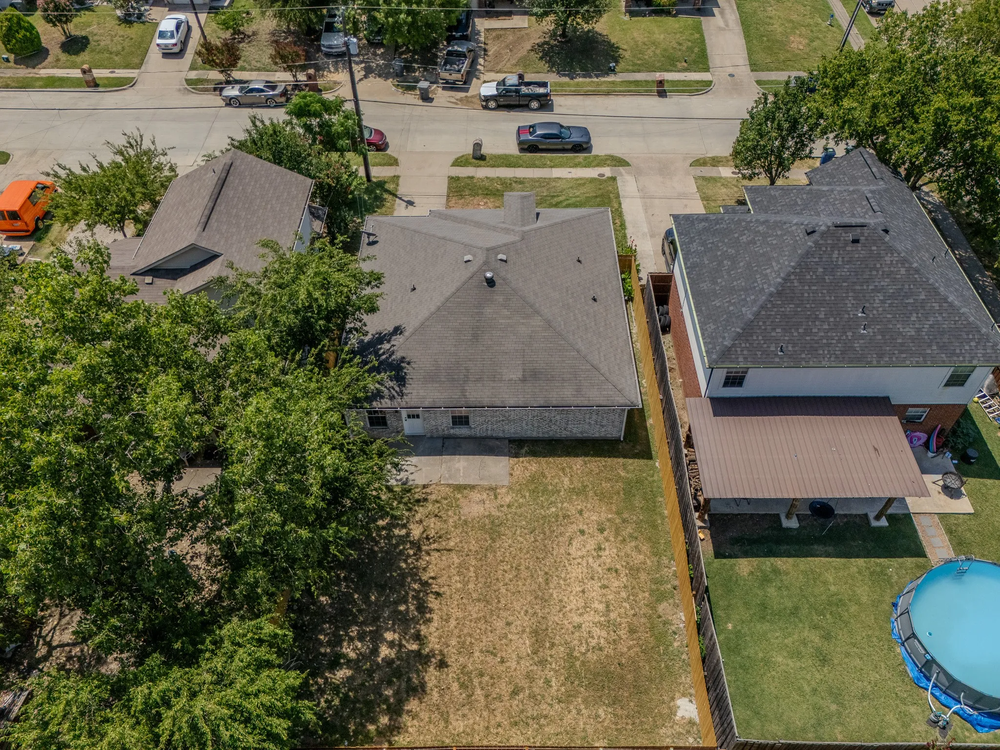 Backyard featuring a privacy fence, mature trees, and a concrete patio with a covered extension