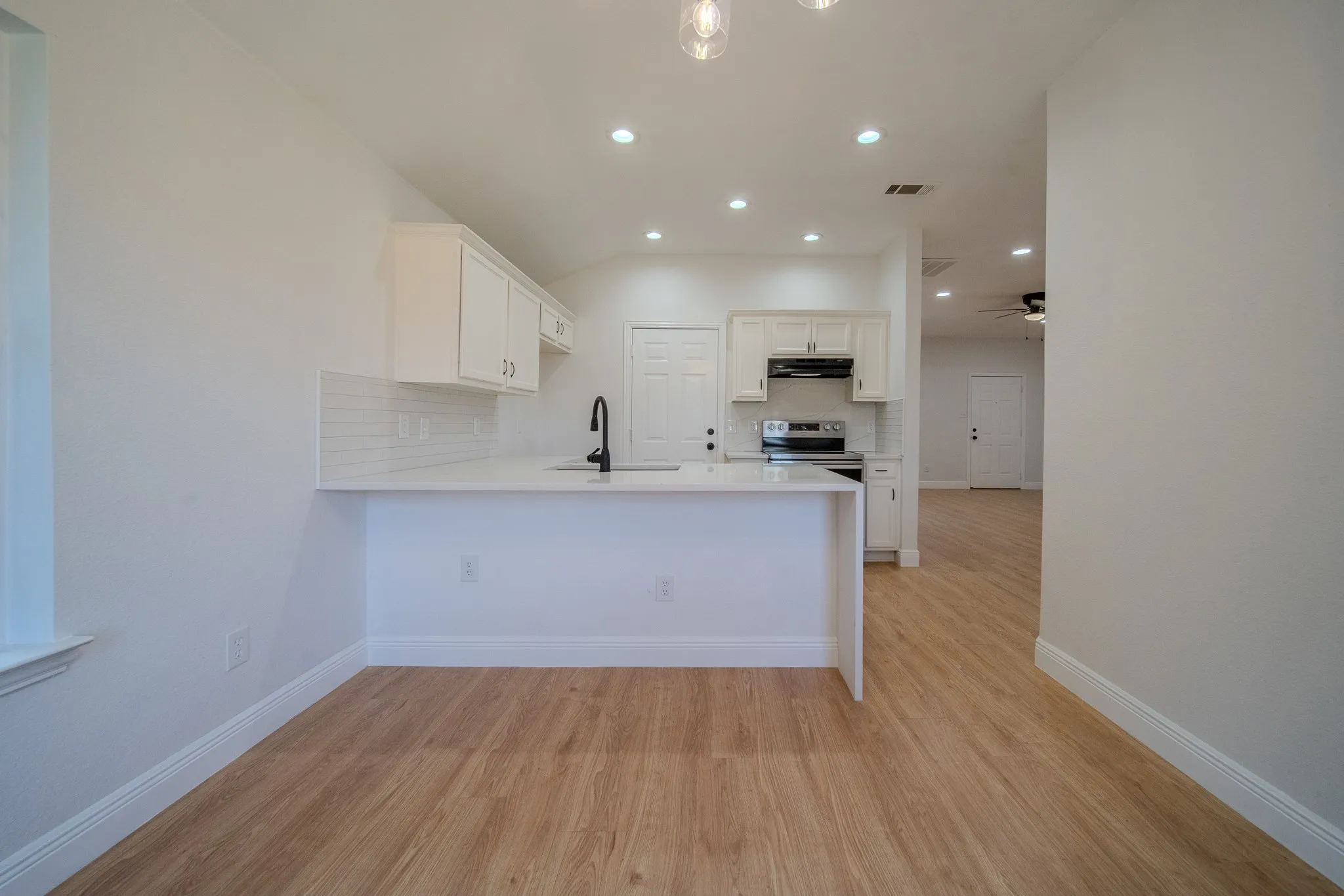 Open-concept kitchen featuring white cabinetry, a built-in stainless steel range with overhead microwave, a white subway tile backsplash, and a breakfast bar with a white countertop