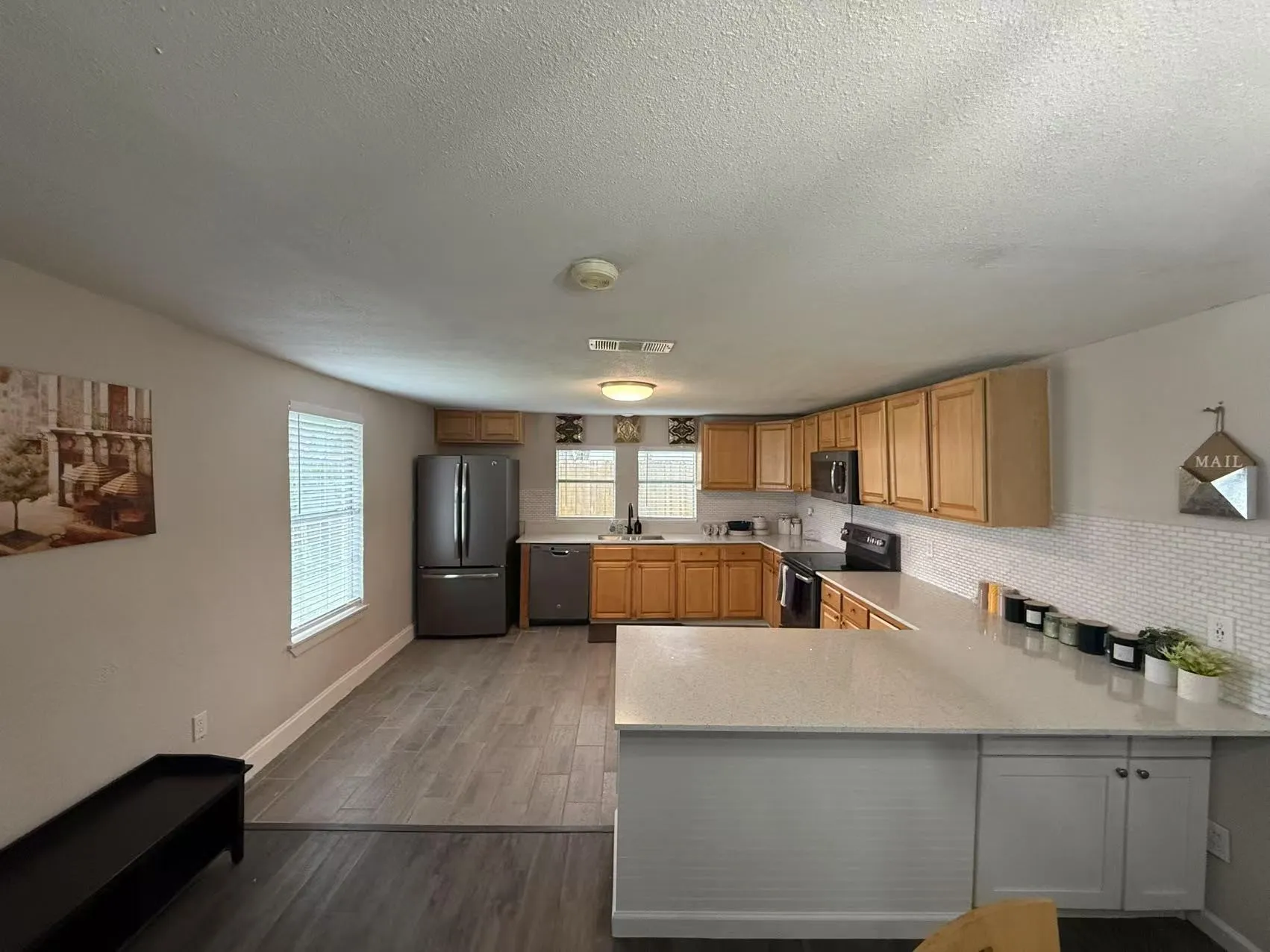 Kitchen with wood-finish flooring, light wood cabinetry, stone-look countertops, and a subway tile backsplash