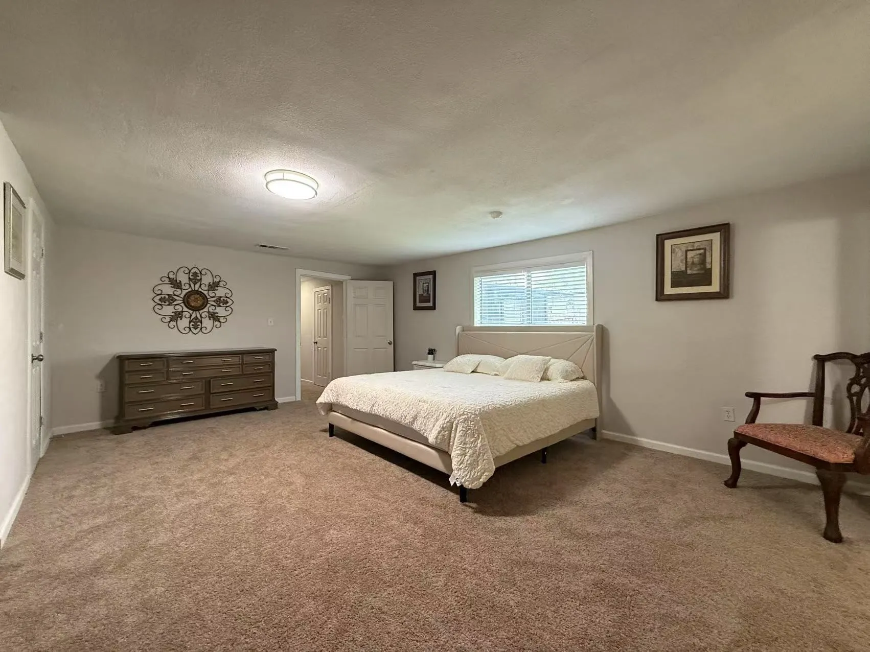 Spacious carpeted room featuring a ceiling-mounted light fixture, light-toned walls, and a window with blinds