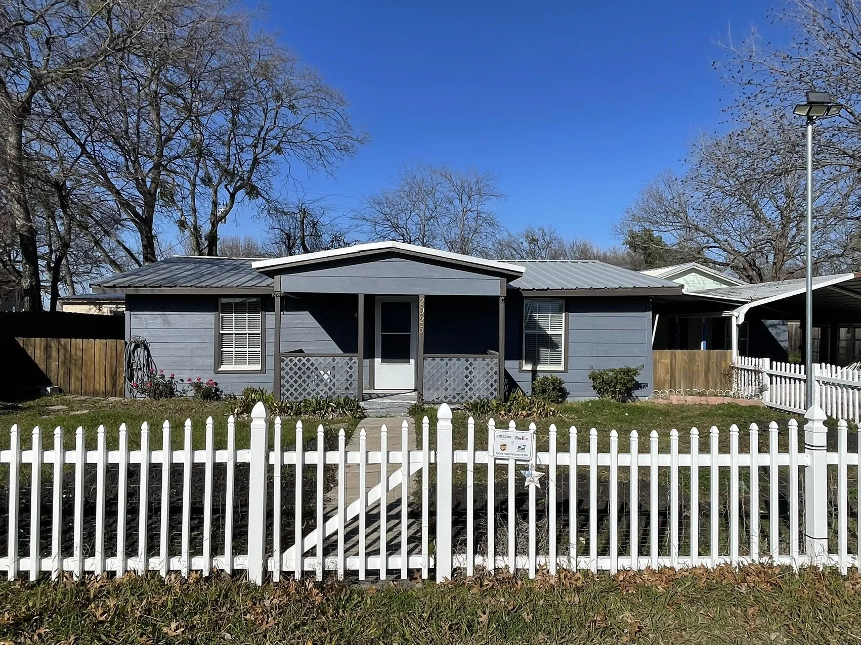 Gray siding exterior featuring a white picket fence, covered front porch, and a metal roof