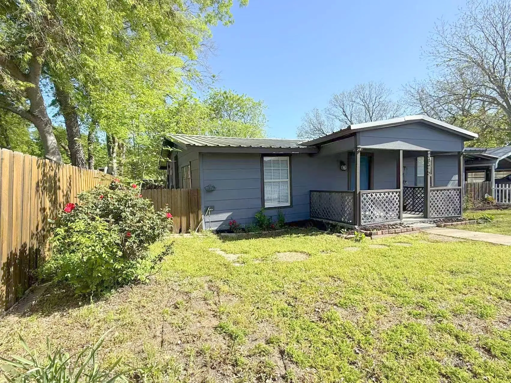 Exterior featuring a covered front porch with lattice railing, a metal roof, and a wood privacy fence
