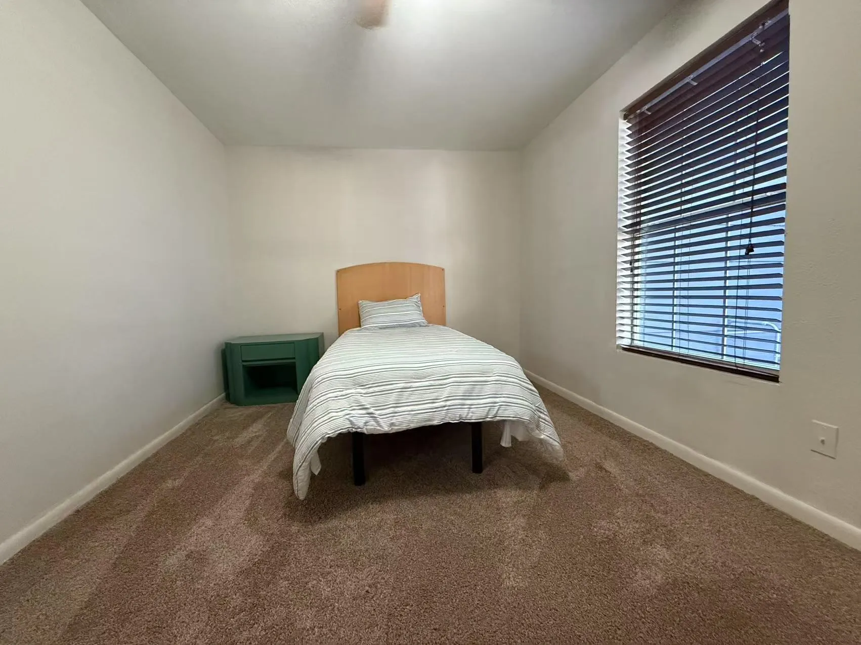 Carpeted room featuring a large window with horizontal blinds, neutral wall paint, and a ceiling fan