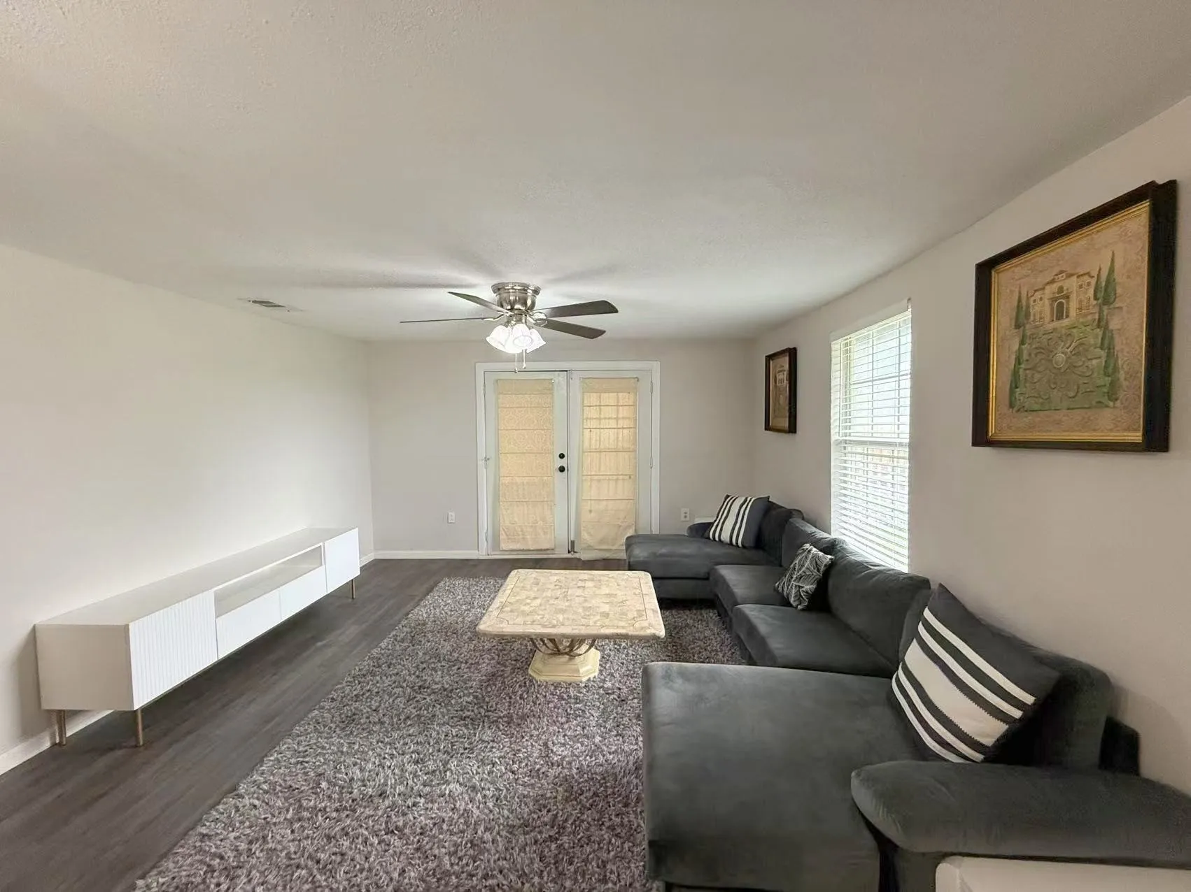Spacious living area featuring dark wood-finish flooring, a ceiling fan with light fixture, and white walls