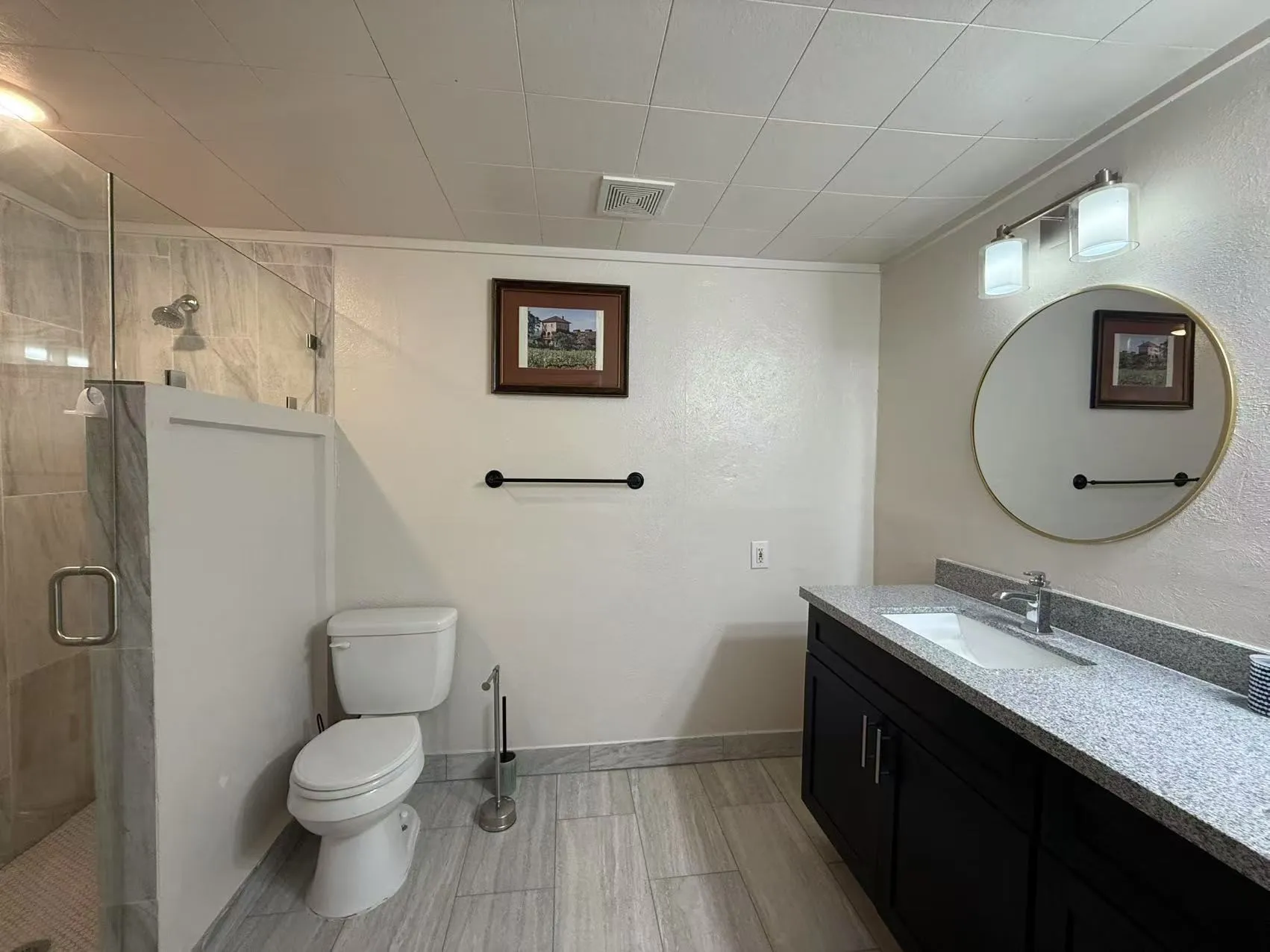Bathroom featuring a dark wood-finish vanity with a light speckled countertop, an undermount sink, and a gold-framed round mirror
