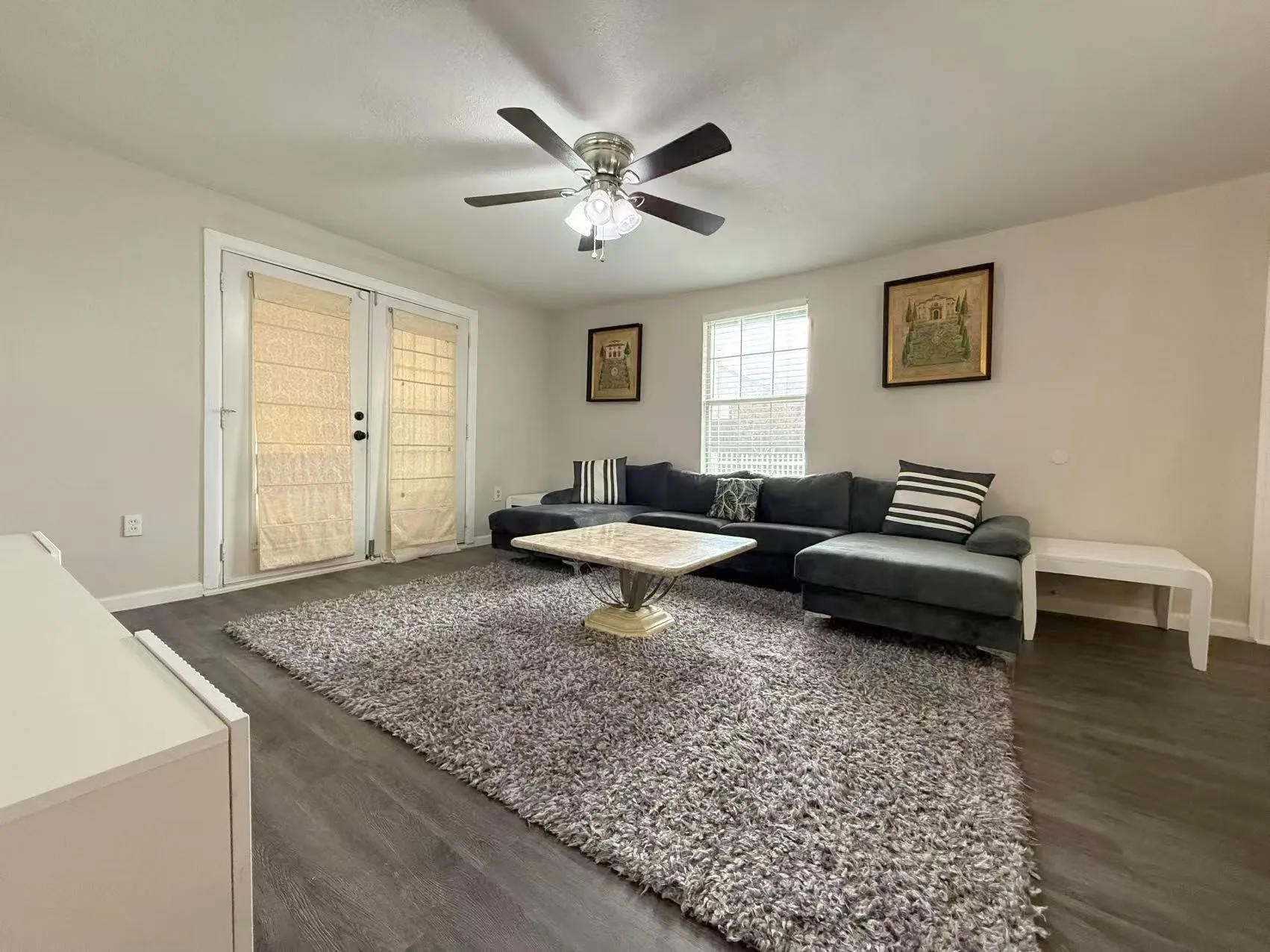 Spacious living area featuring modern wood-finish flooring, a ceiling fan with light fixture, and light-colored walls