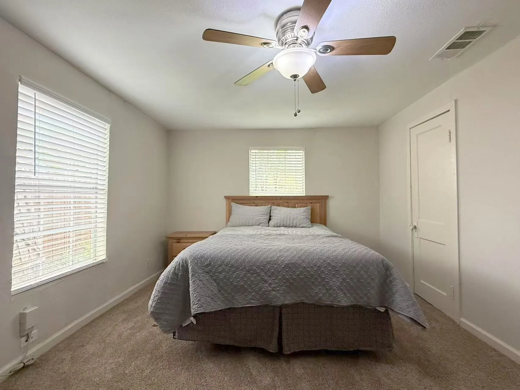 Carpeted room featuring a ceiling fan with light fixture, two windows with blinds, and a paneled door