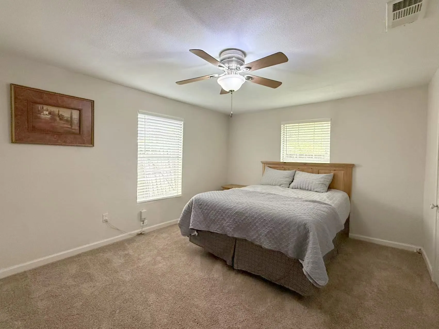 Carpeted room featuring a ceiling fan with light fixture, two windows with horizontal blinds, and white baseboards