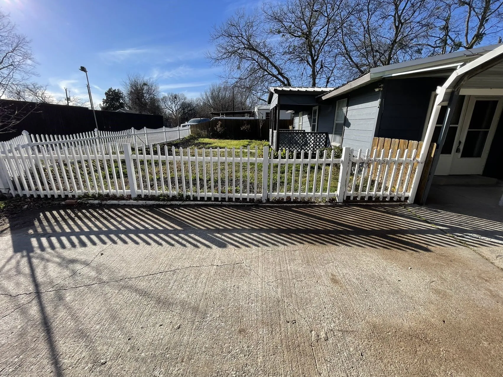 Front yard featuring a white picket fence, concrete driveway, and partial exterior siding