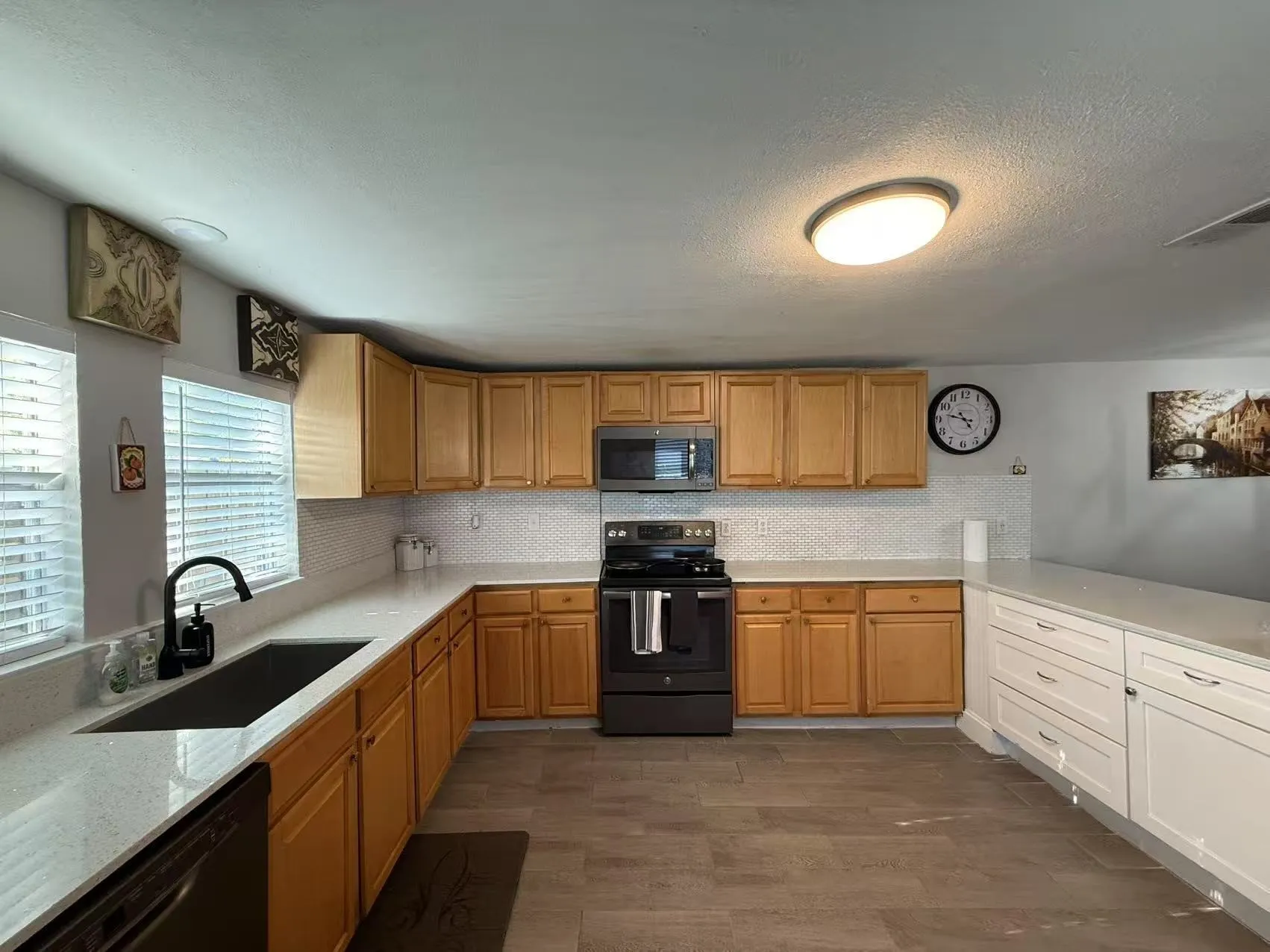 Spacious kitchen featuring light wood cabinetry, light countertops, black range, built-in microwave, and wood-finish flooring