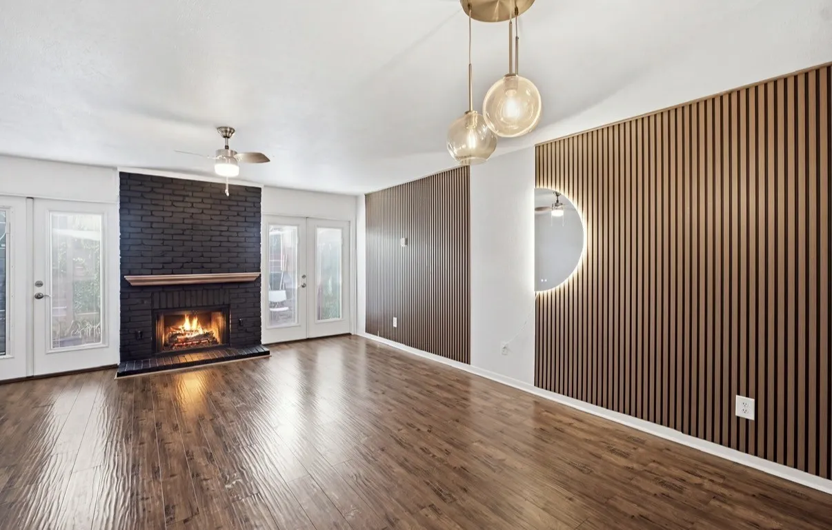 Wood-finish flooring, black brick fireplace with wood mantel, ceiling fan, and dual glass paneled doors
