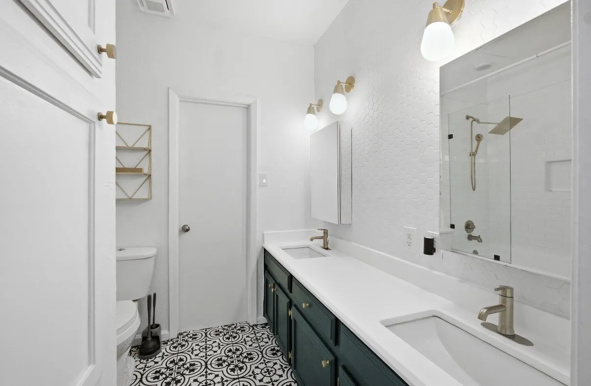 Double vanity with integrated sinks, patterned floor tile, white hexagonal wall tile, contemporary light fixtures, and a shower with a rainfall showerhead