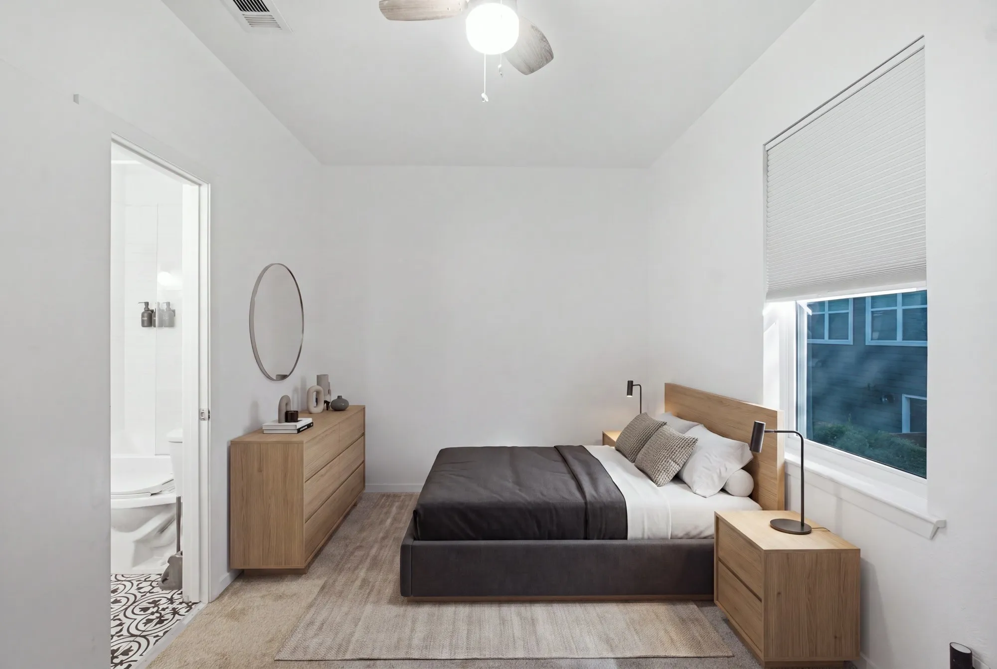 White walls, wood-finish flooring, ceiling fan with integrated lighting, window with cellular shades, and an attached bathroom with patterned tile flooring