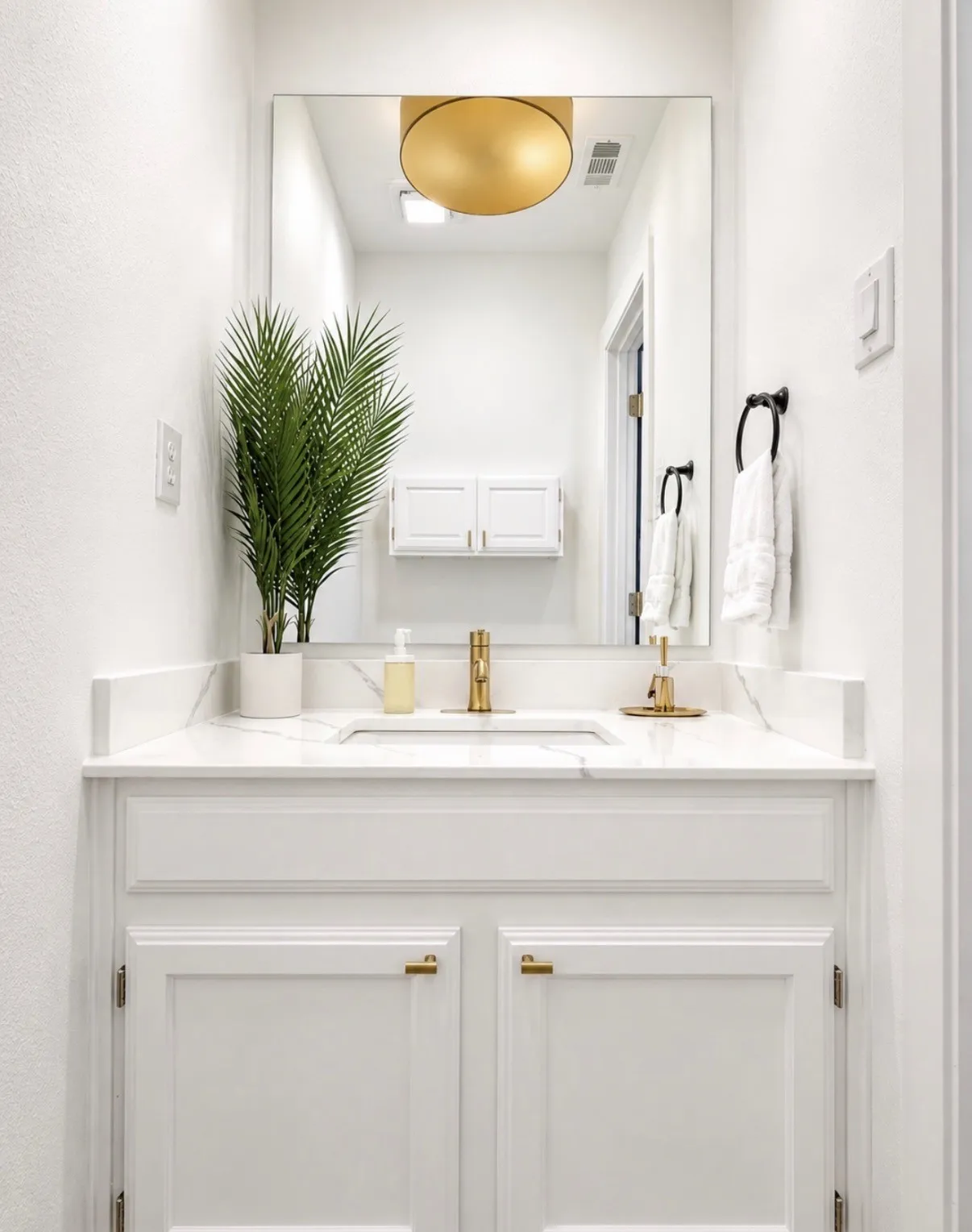 Vanity with a white finish, a single basin sink, a gold-toned faucet, and a large wall-mounted mirror