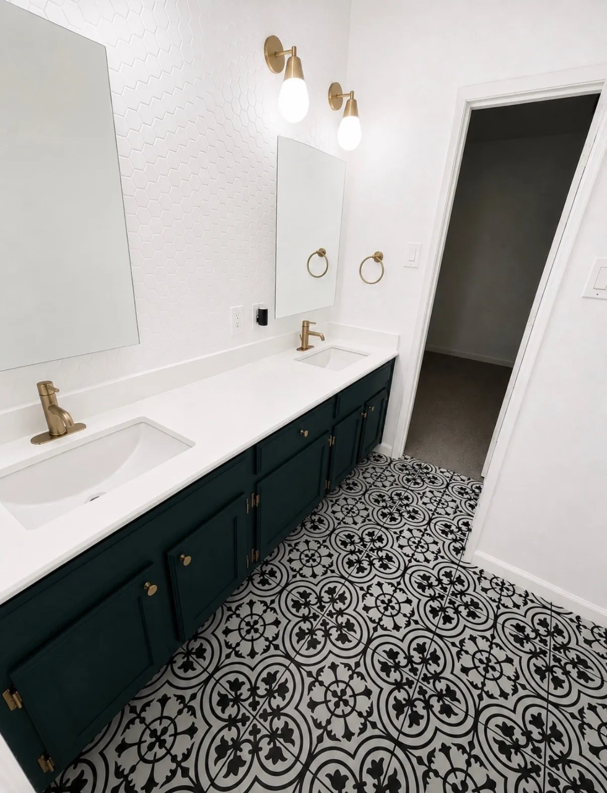 Dual sink vanity with gold-tone hardware, patterned floor tiling, and a textured accent wall