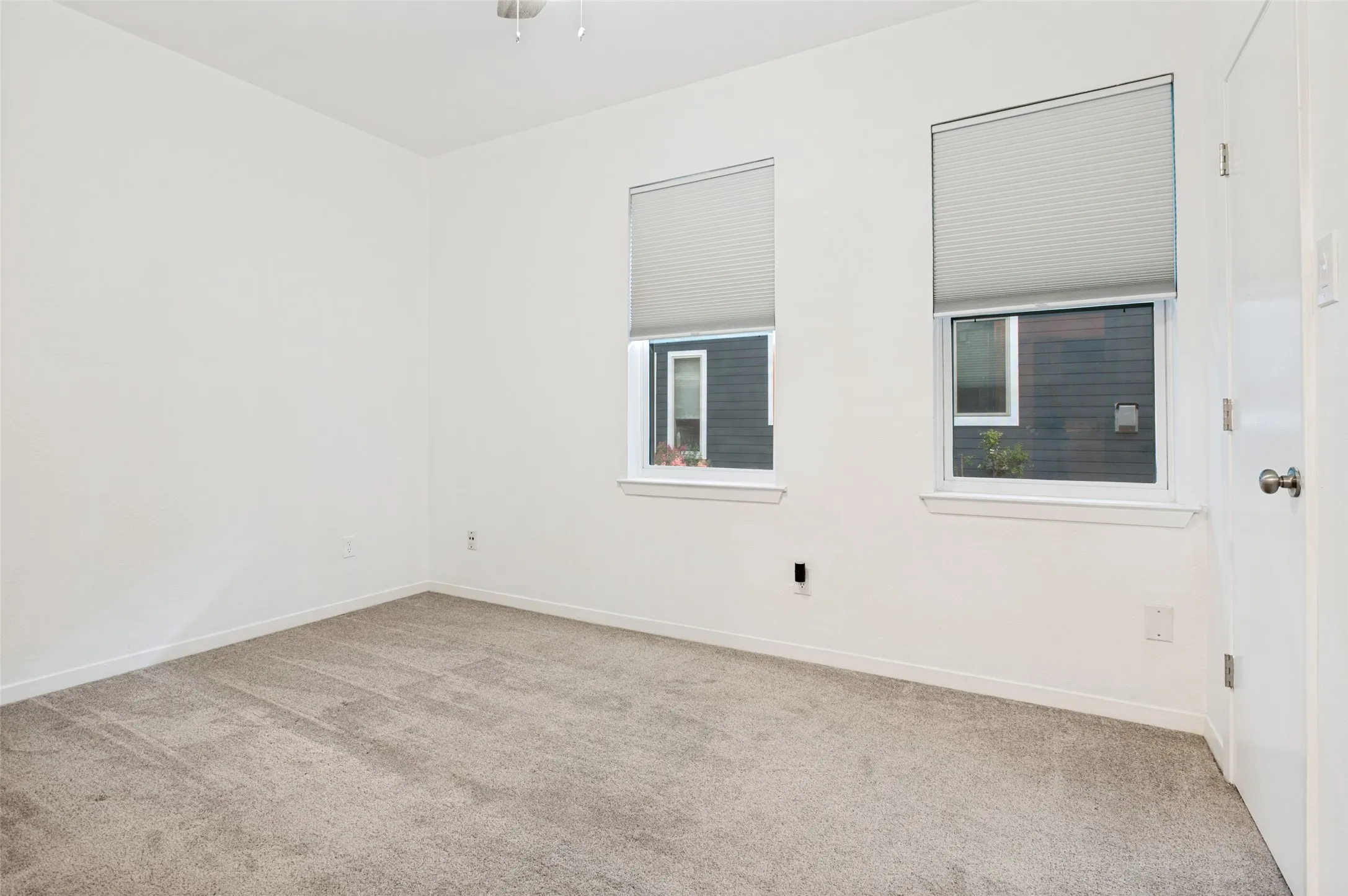 Neutral carpeting, bright white walls, two windows, two window treatments, and a ceiling fan