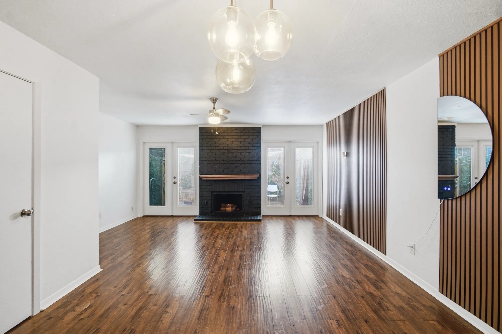 Wood-finish flooring throughout, a black brick fireplace with a wood mantel, and multiple glass-paned doors