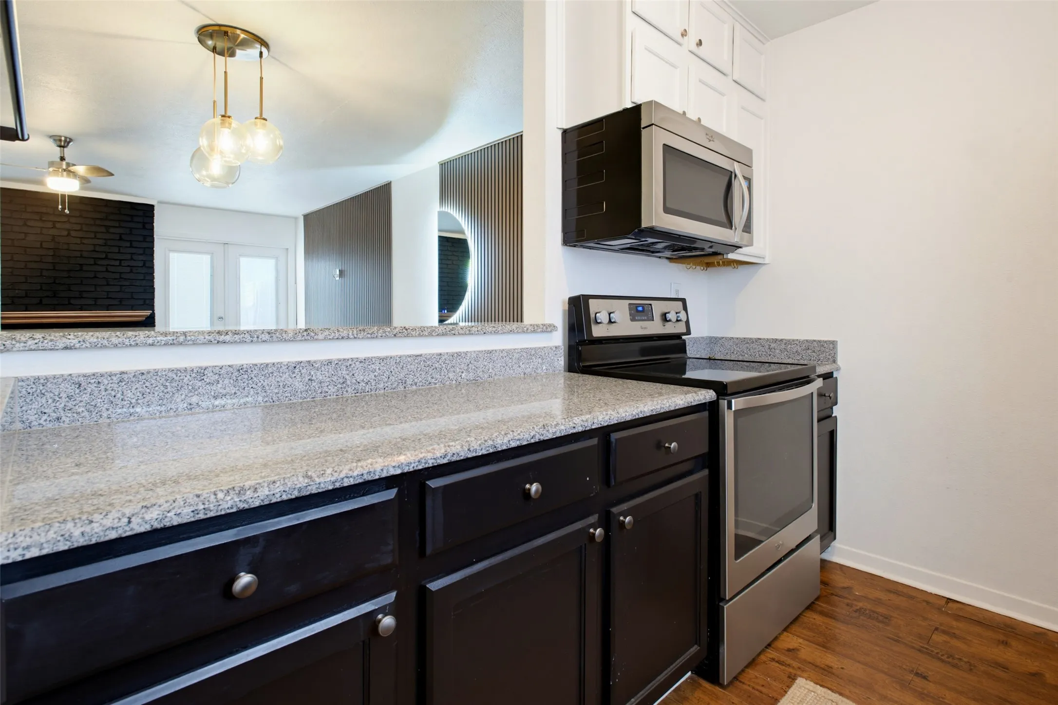 Granite-finish countertops, stainless steel appliances, dark wood-finish cabinetry, and overhead pendant lighting