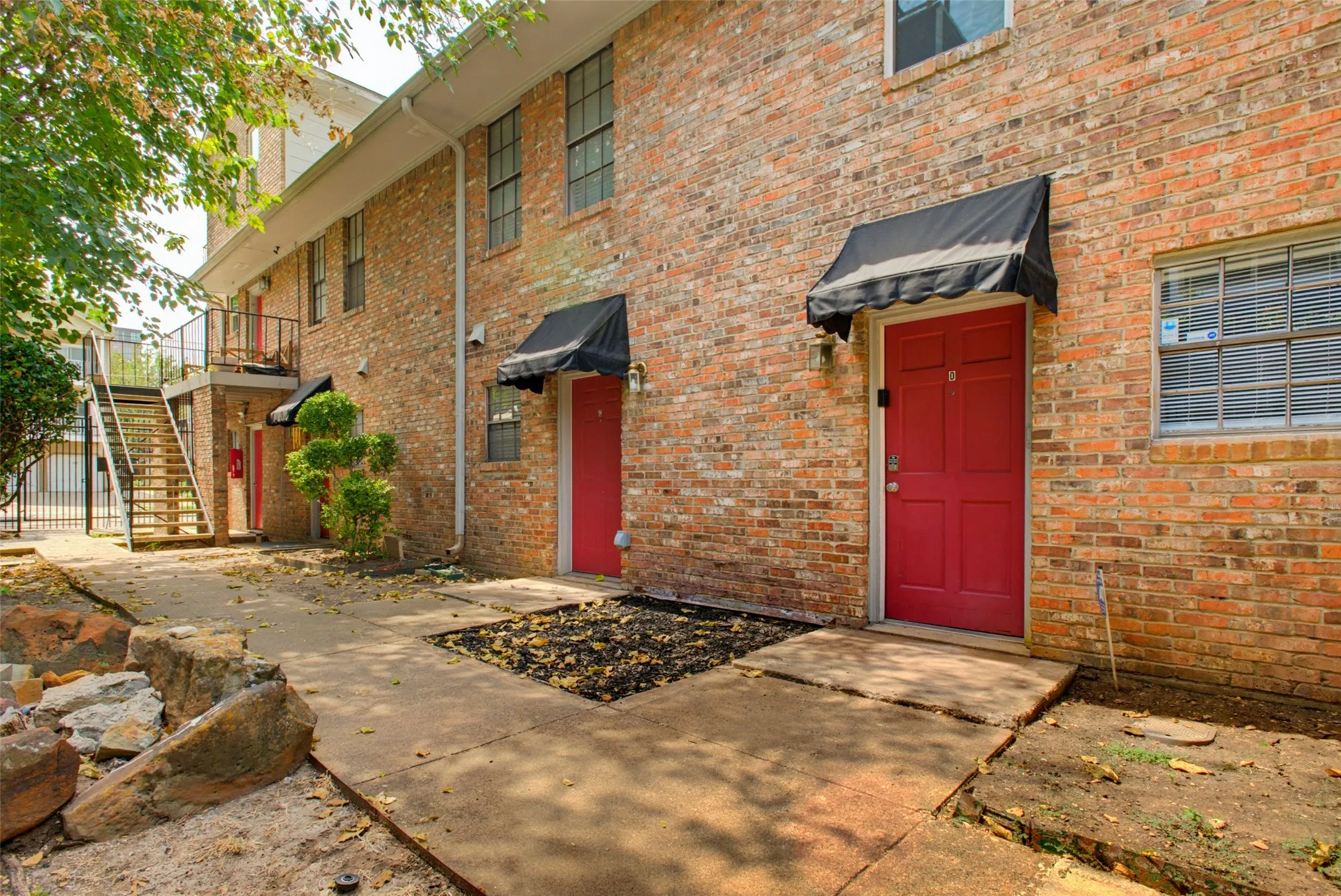 Brick exterior with red entry doors, black awnings, and an exterior metal staircase