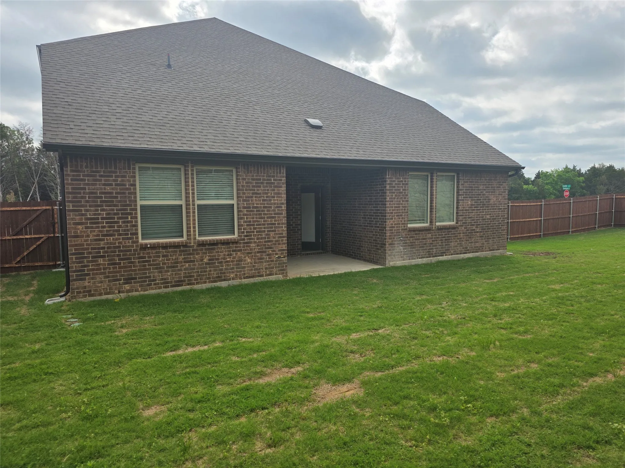 Expansive backyard featuring a manicured lawn, full privacy fencing, brick exterior, and a covered patio