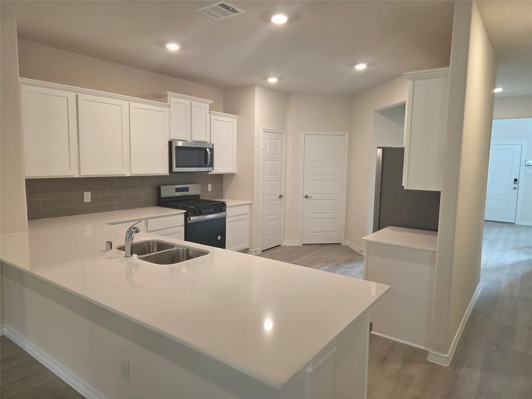 Kitchen featuring white cabinetry, light-toned countertops, a stainless steel sink with a chrome faucet, a gas range, and a built-in microwave